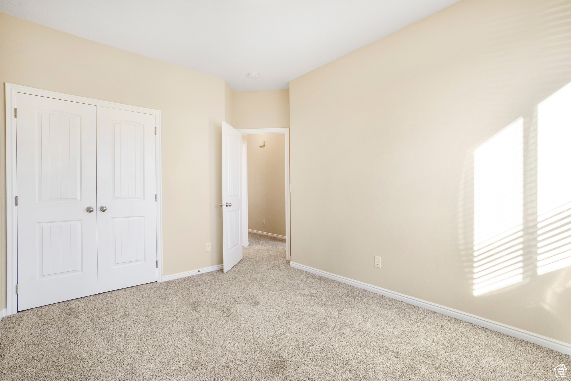 Unfurnished bedroom with light carpet, a closet, and baseboards