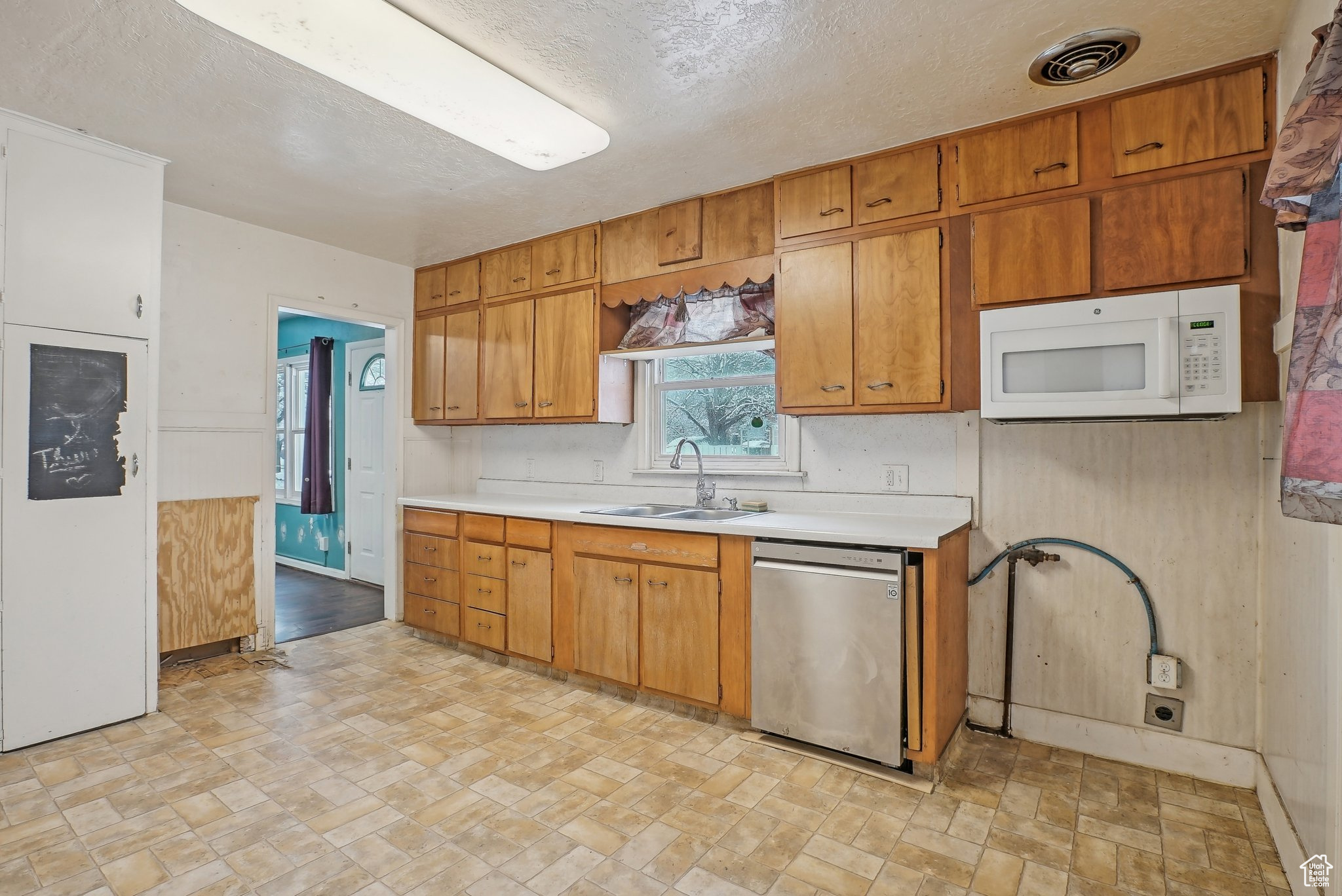 Kitchen with white microwave, a sink, visible vents, light countertops, and stainless steel dishwasher