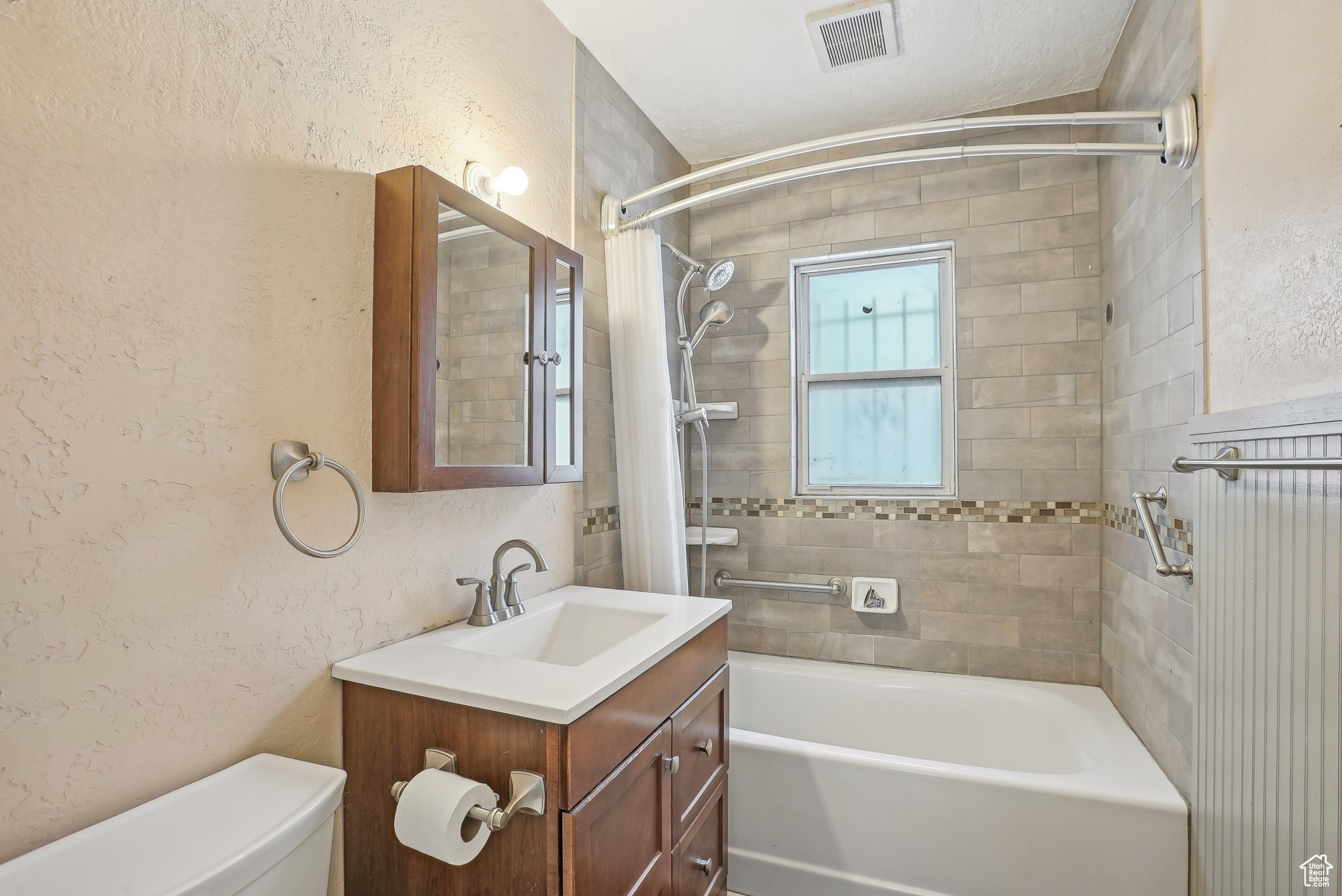 Bathroom with bathing tub / shower combination, visible vents, a textured wall, toilet, and vanity