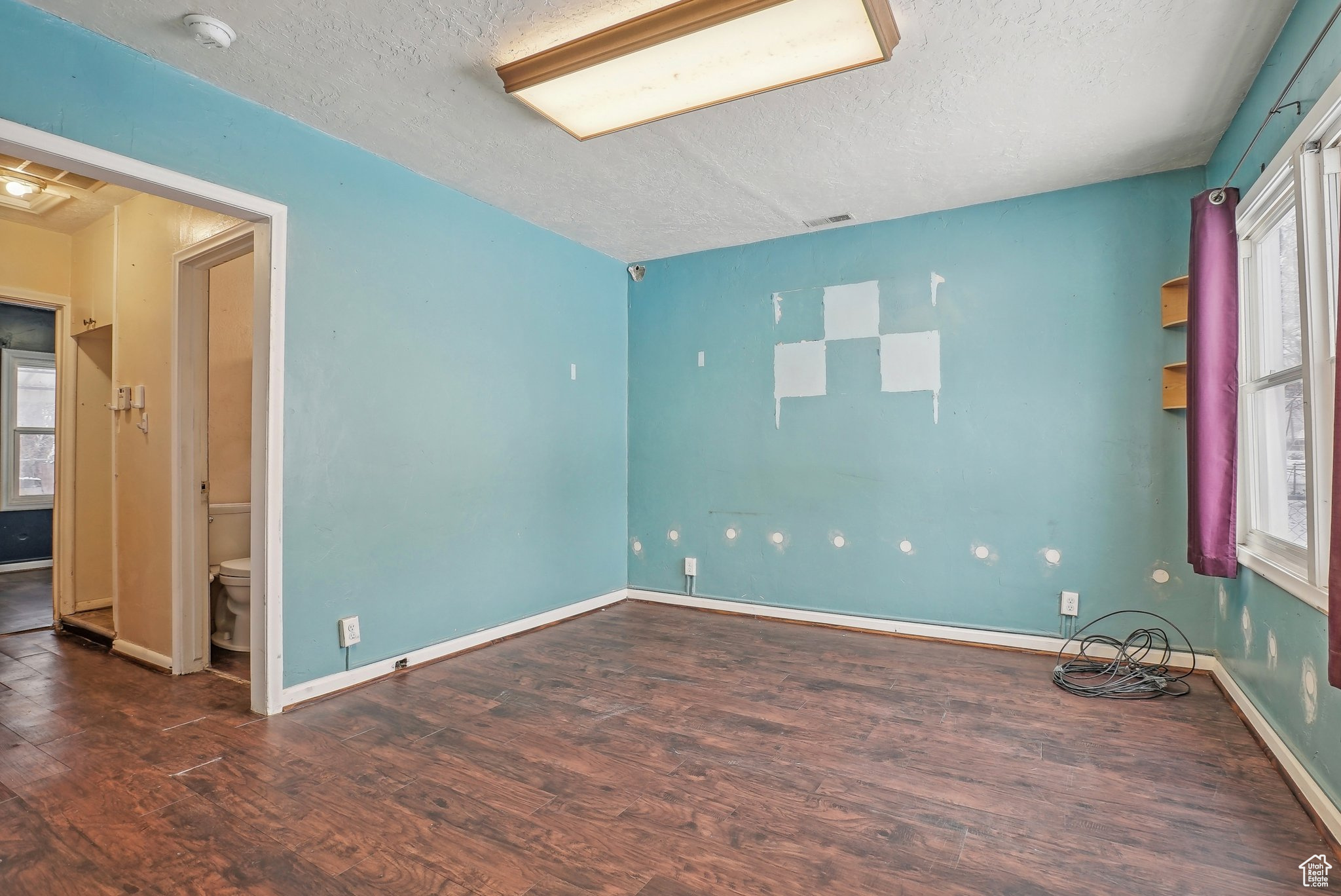 Unfurnished room featuring baseboards, visible vents, dark wood finished floors, and a textured ceiling