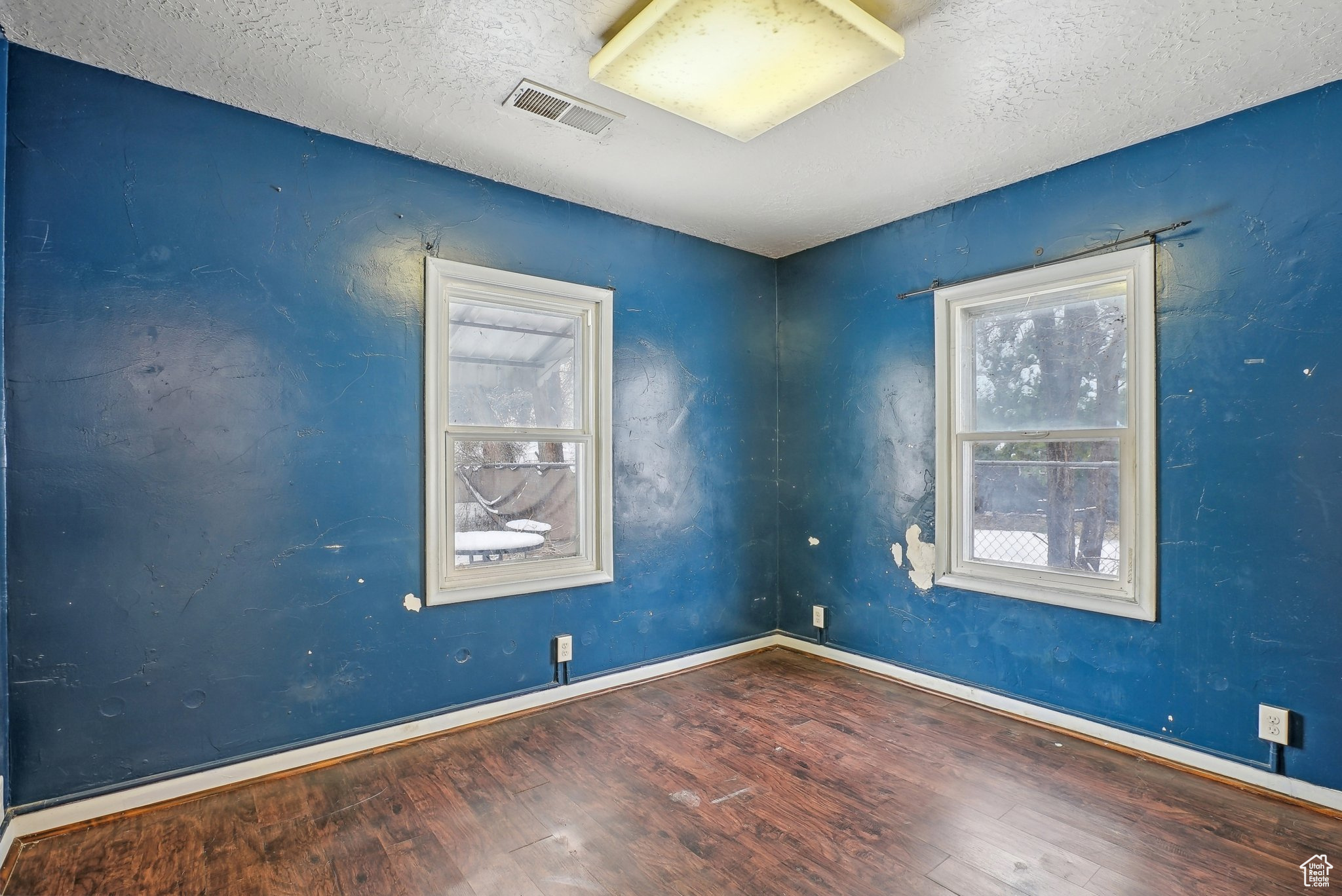 Empty room featuring a textured ceiling, wood finished floors, visible vents, and baseboards