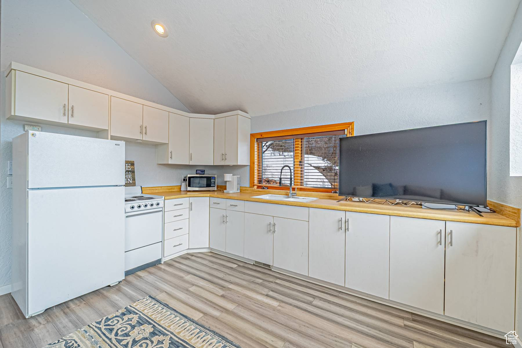Kitchen featuring lofted ceiling, white appliances, a sink, white cabinets, and light countertops