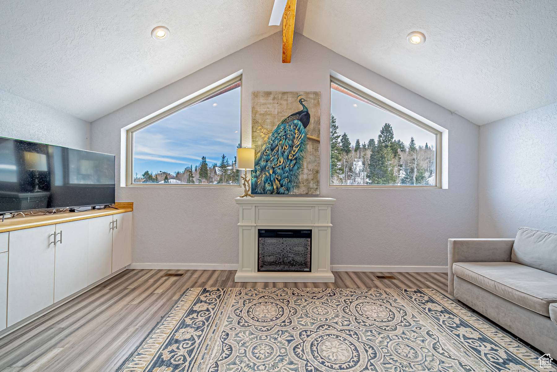 Living area featuring a fireplace with raised hearth, light wood finished floors, a textured ceiling, and baseboards