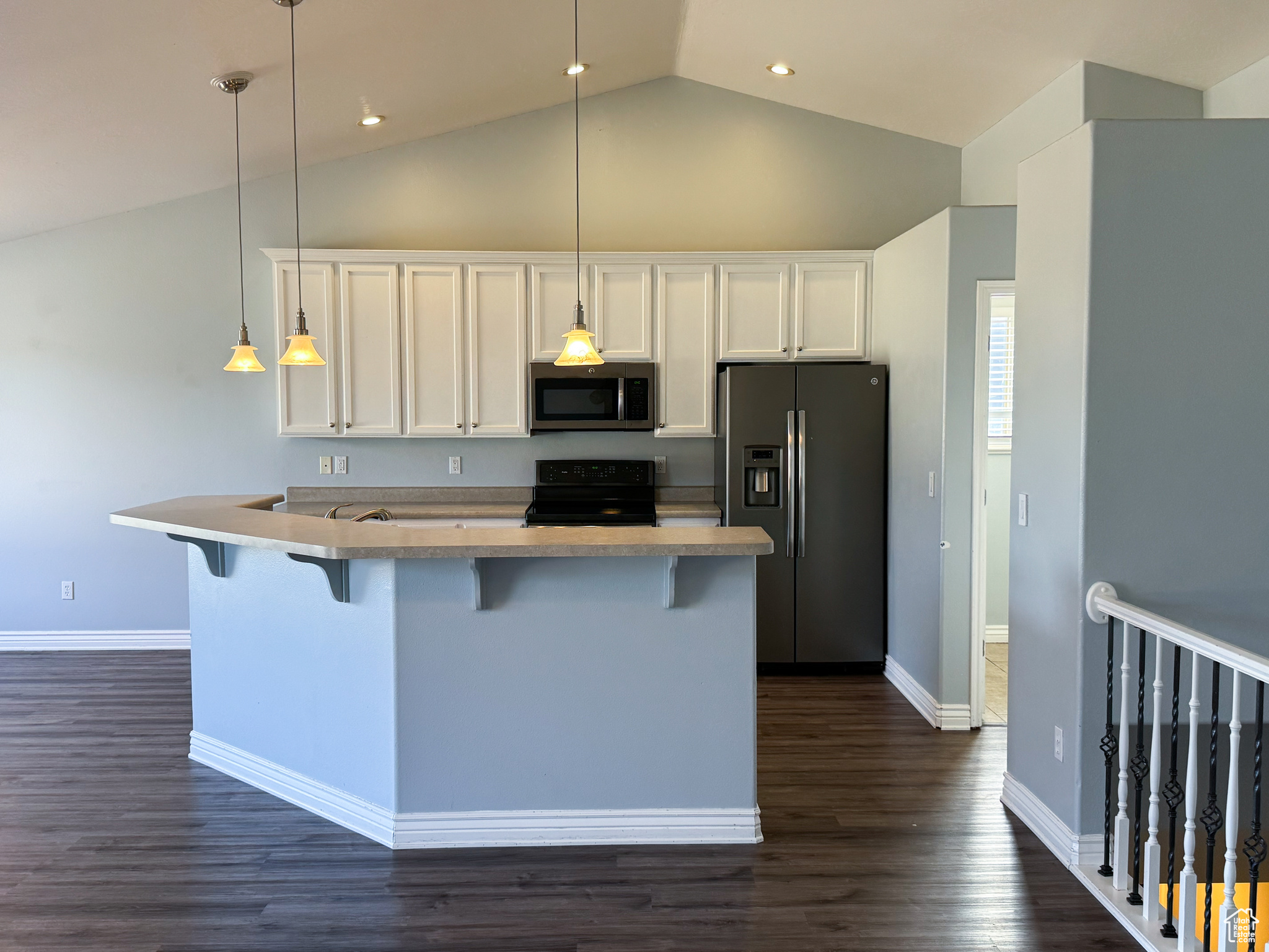 Kitchen featuring white cabinets, dark wood-style floors, hanging light fixtures, stainless steel appliances, and a kitchen bar