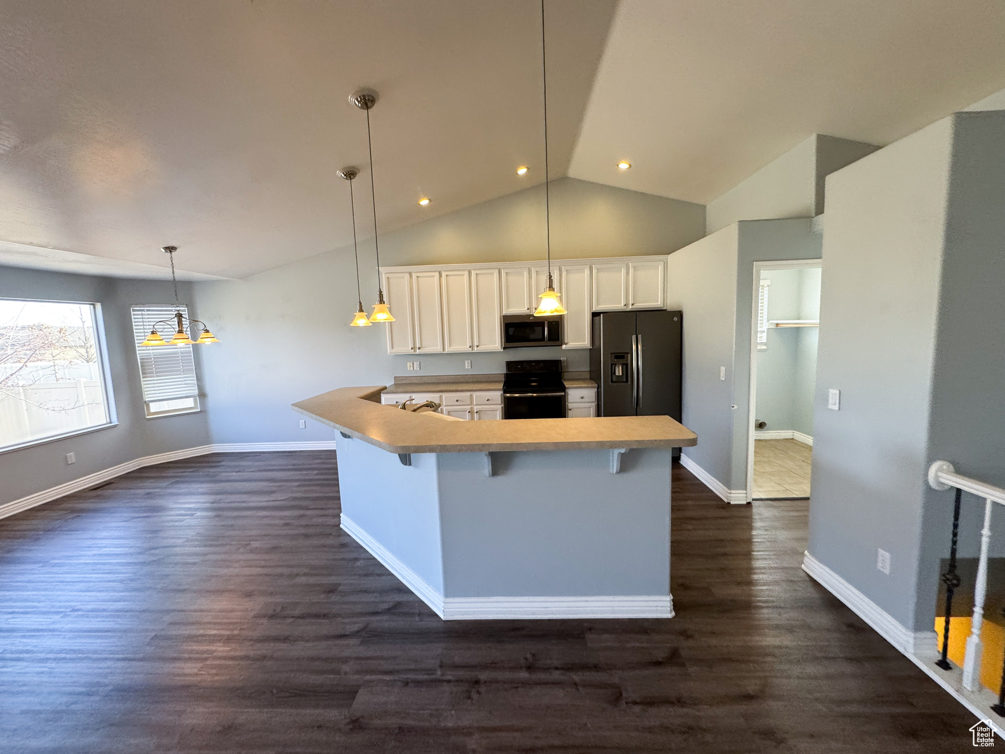 Kitchen featuring stainless steel appliances, a breakfast bar, dark wood-type flooring, white cabinetry, and hanging light fixtures
