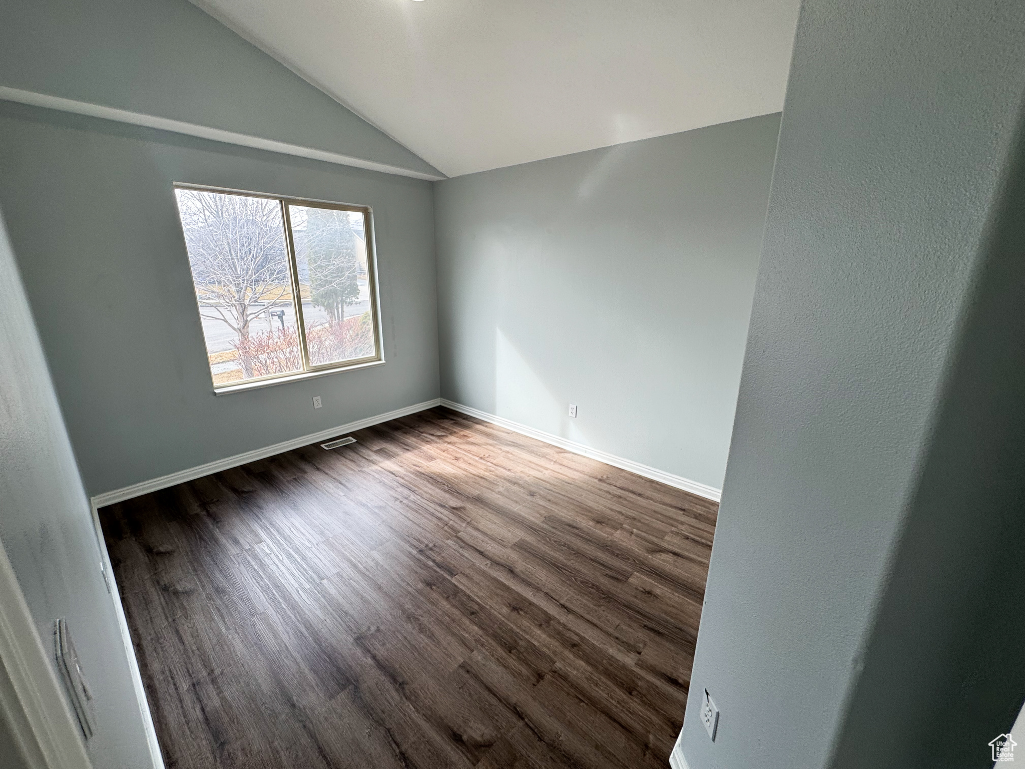 Spare room featuring dark wood-style flooring, visible vents, vaulted ceiling, and baseboards