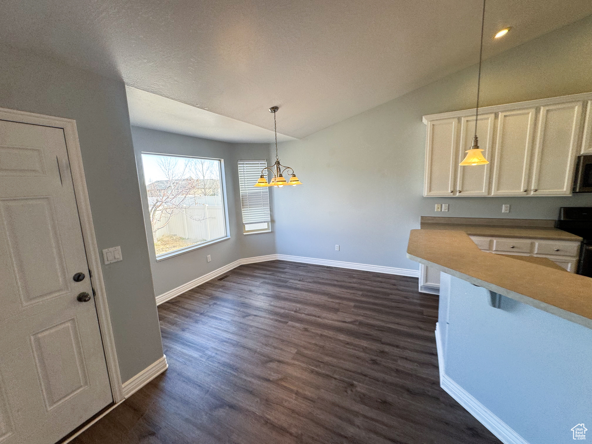 Kitchen featuring decorative light fixtures, stainless steel appliances, light countertops, white cabinetry, and vaulted ceiling
