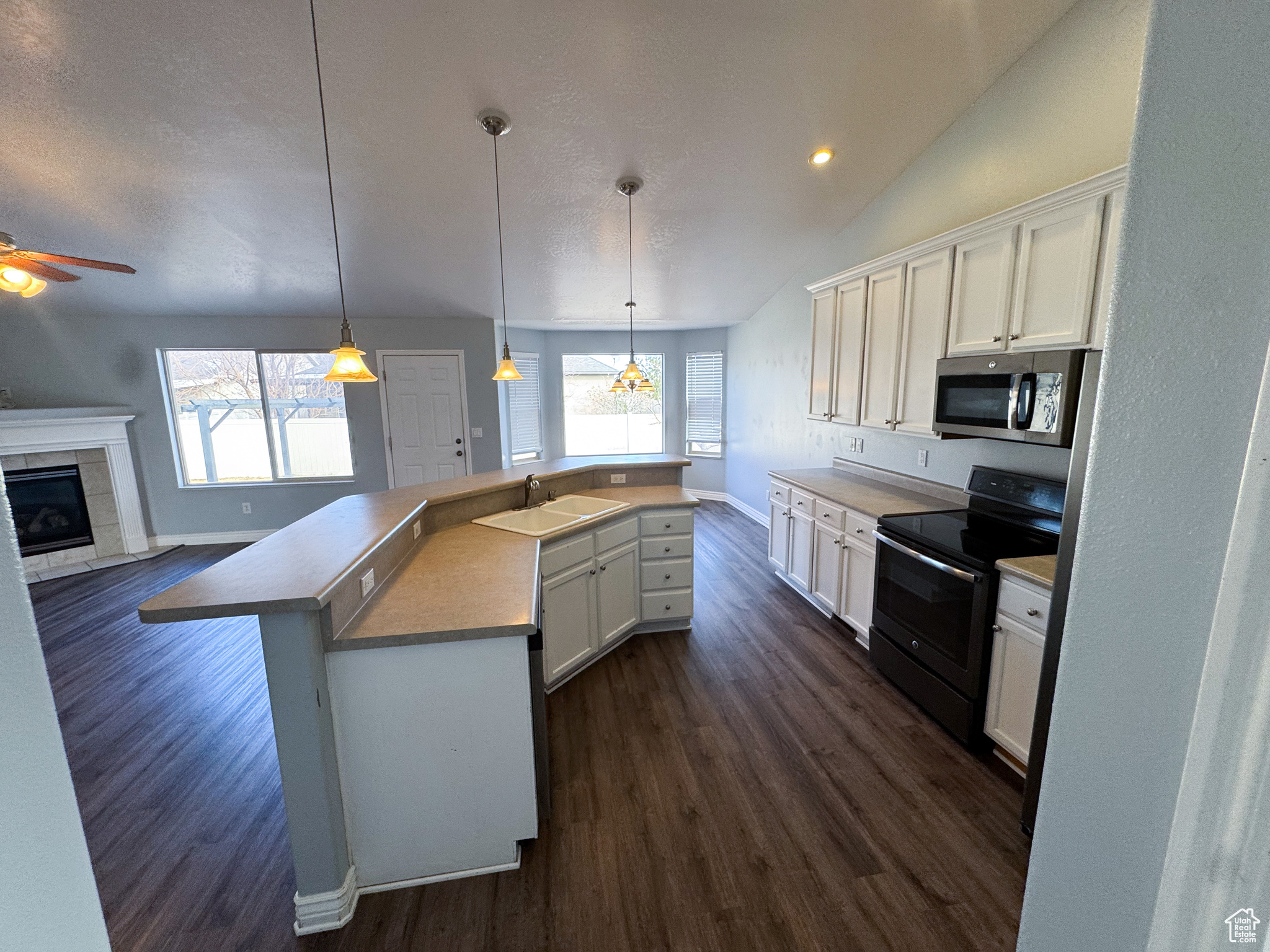 Kitchen with electric range, white cabinetry, a center island with sink, stainless steel microwave, and decorative light fixtures