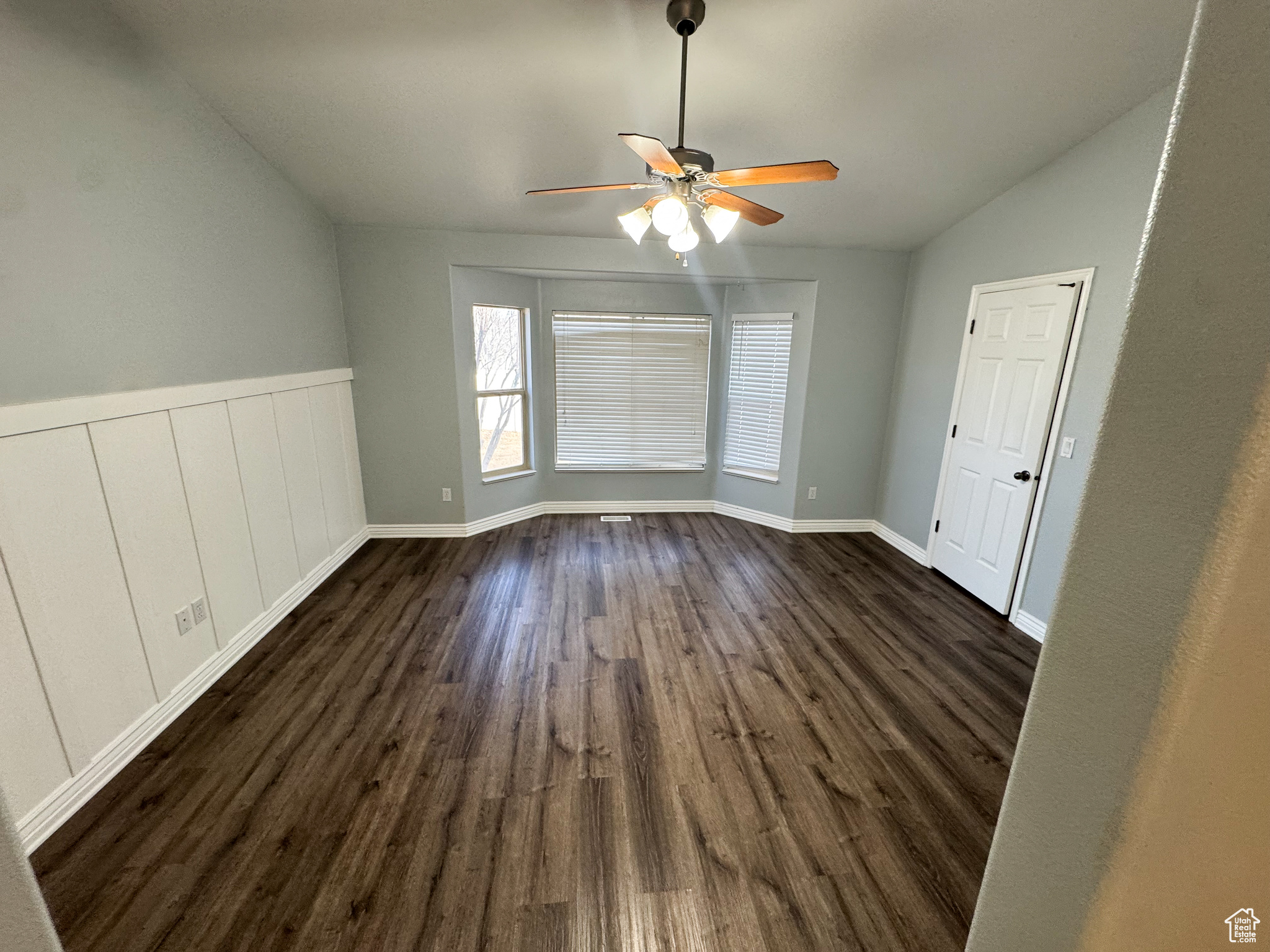Spare room with a ceiling fan, lofted ceiling, wainscoting, and dark wood finished floors