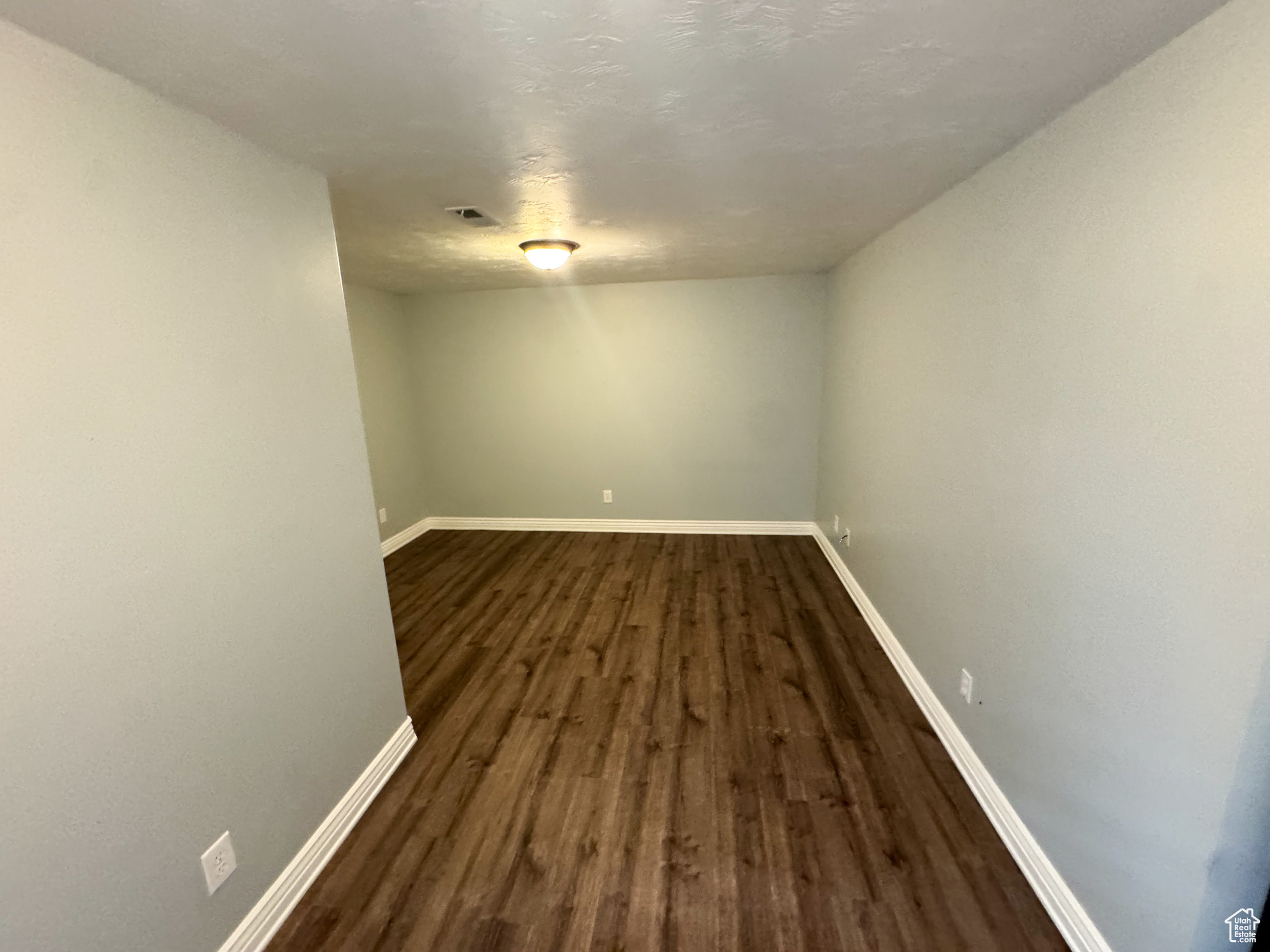 Spare room featuring dark wood-style flooring, visible vents, and baseboards