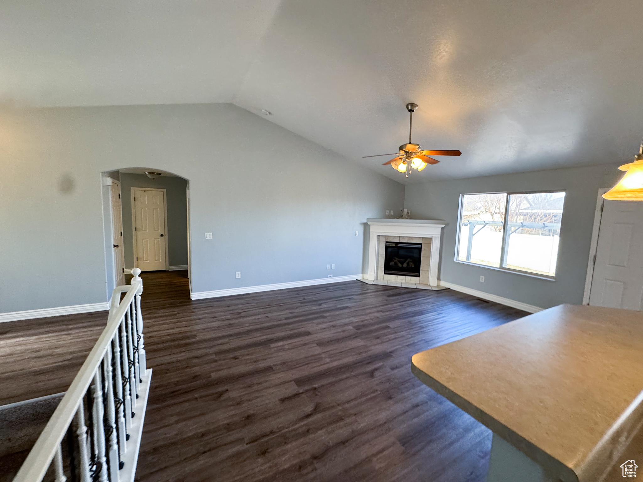 Unfurnished living room with arched walkways, ceiling fan, a tile fireplace, vaulted ceiling, and dark wood finished floors