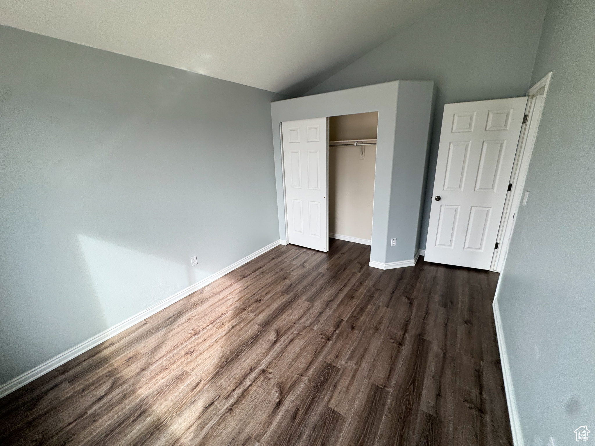 Unfurnished bedroom with lofted ceiling, dark wood-style floors, baseboards, and a closet