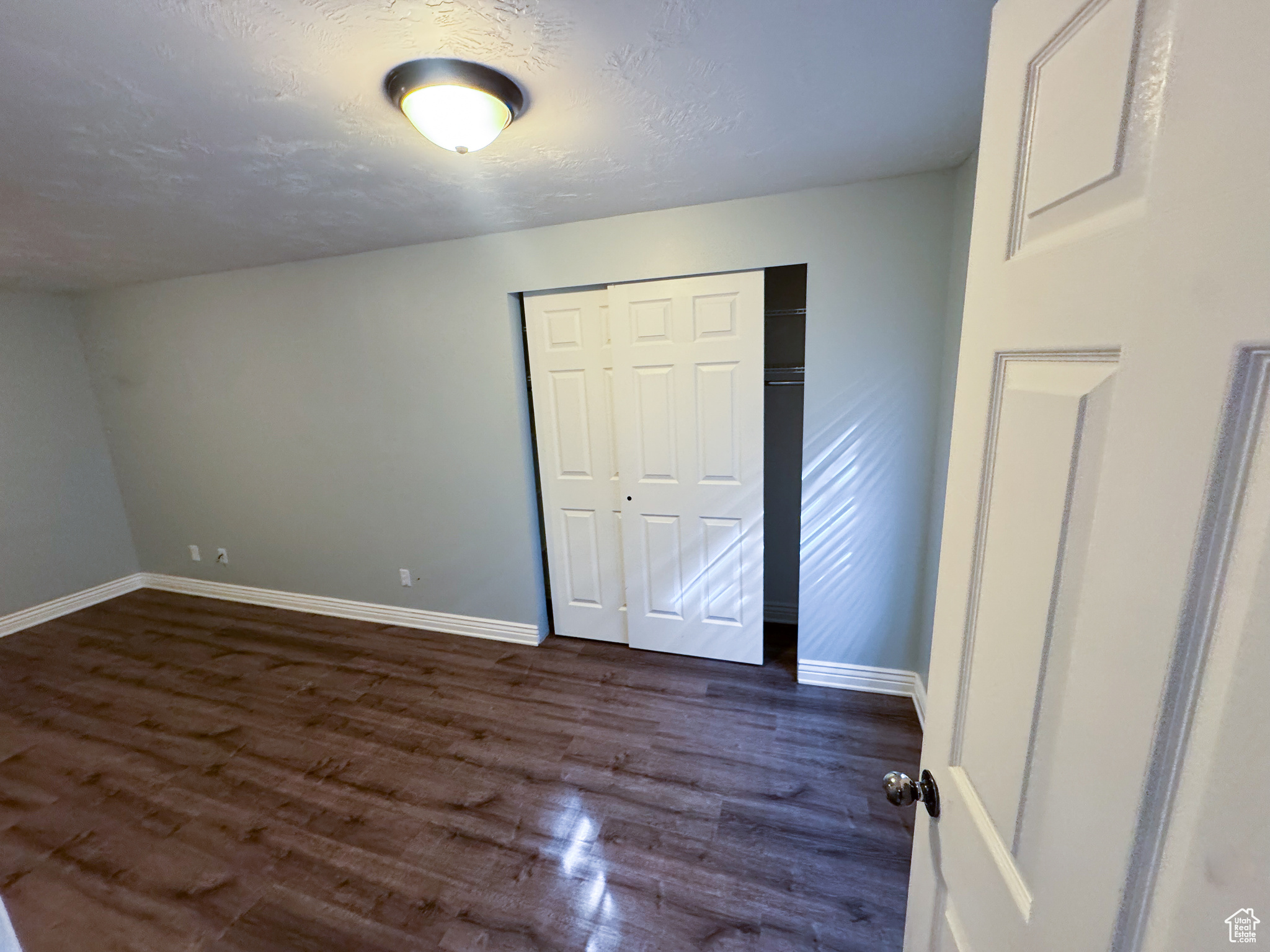 Unfurnished bedroom featuring a closet, dark wood finished floors, a textured ceiling, and baseboards