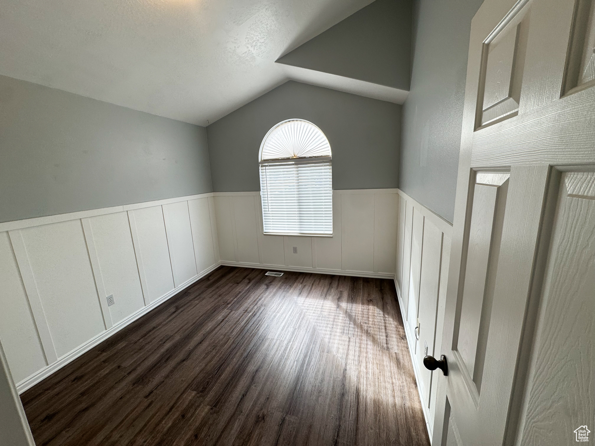 Empty room featuring dark wood finished floors, a wainscoted wall, and vaulted ceiling