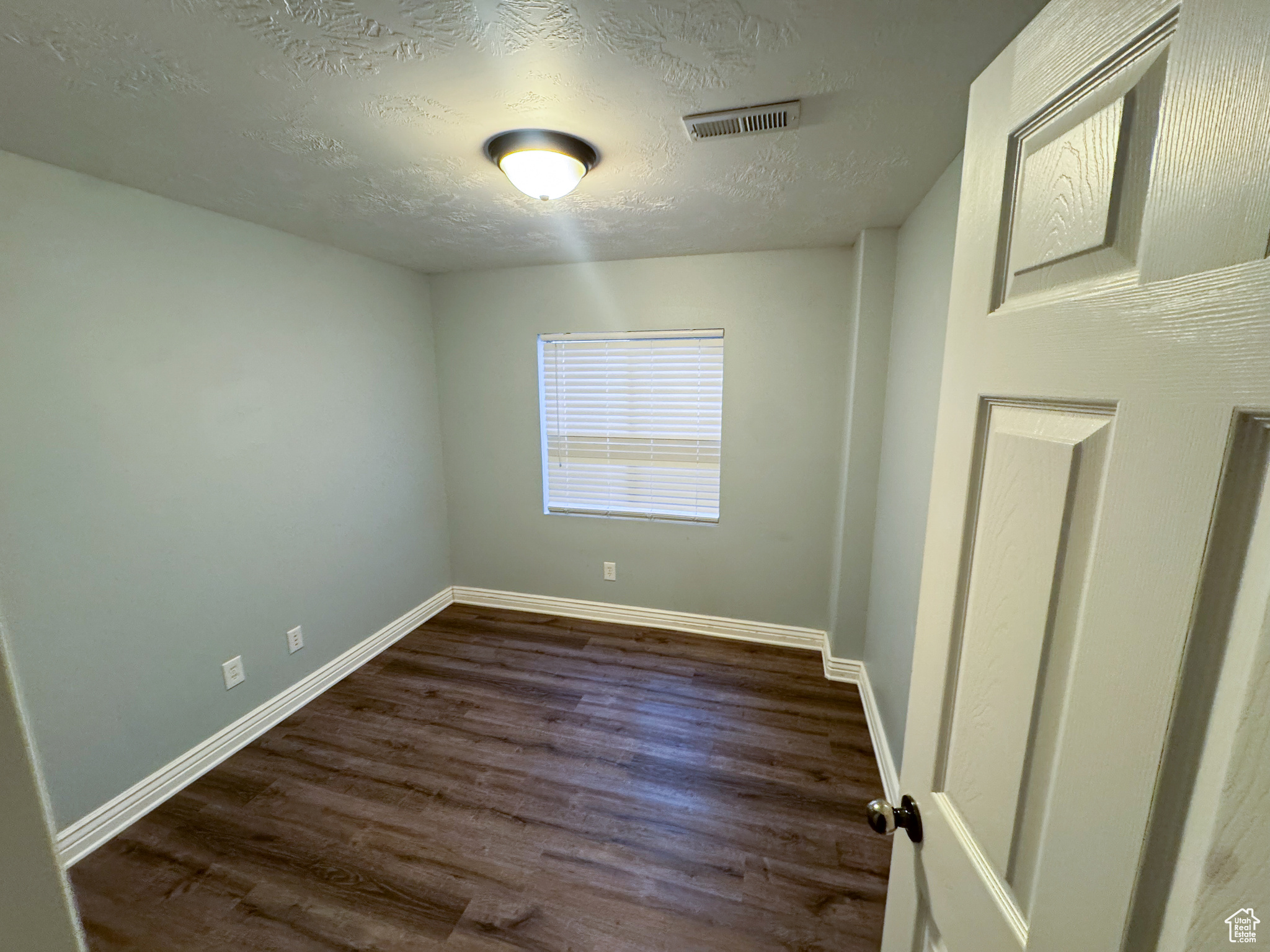 Unfurnished room with a textured ceiling, dark wood finished floors, visible vents, and baseboards