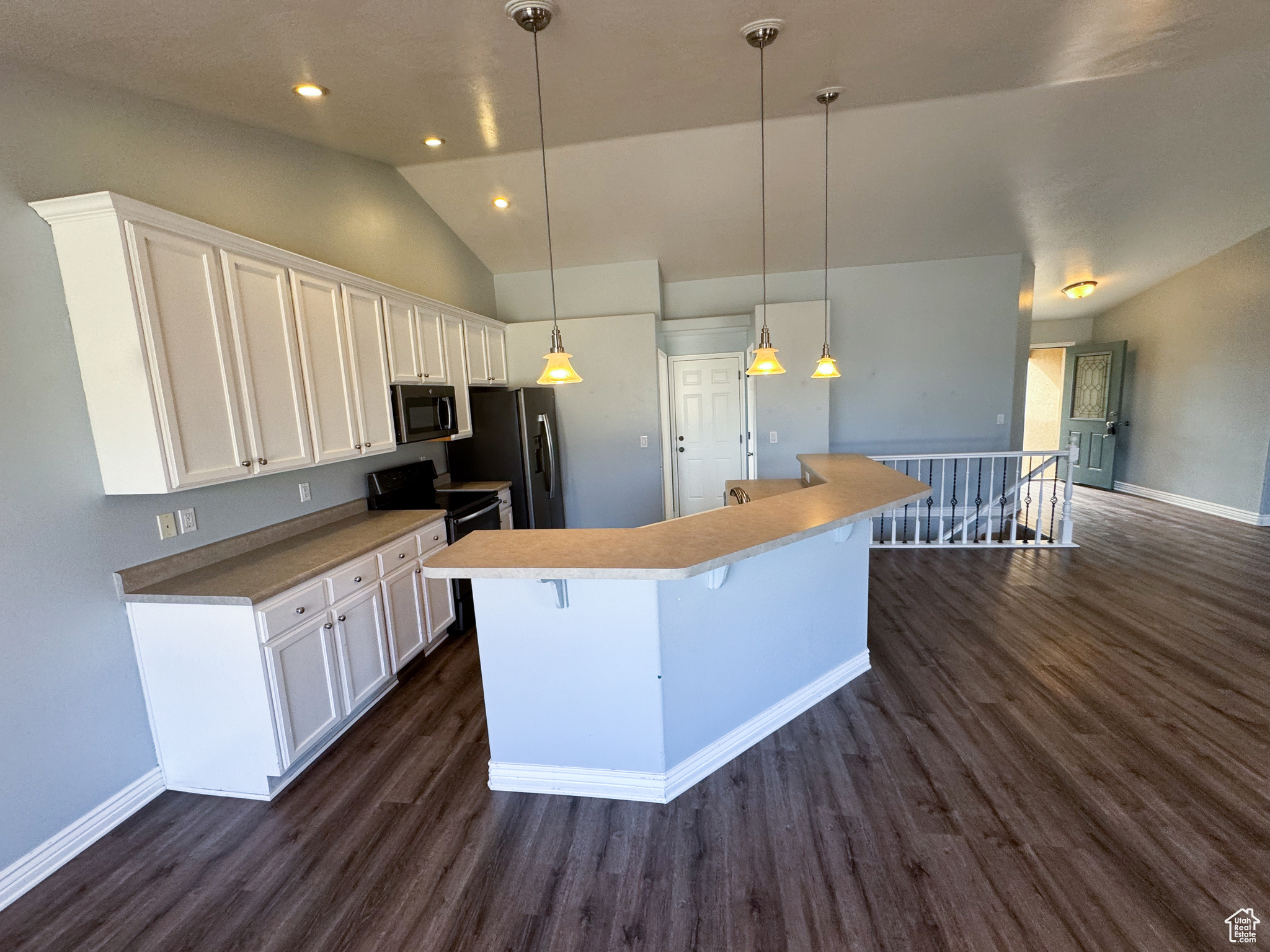 Kitchen with stainless steel fridge, a kitchen island, black electric range oven, decorative light fixtures, and white cabinetry