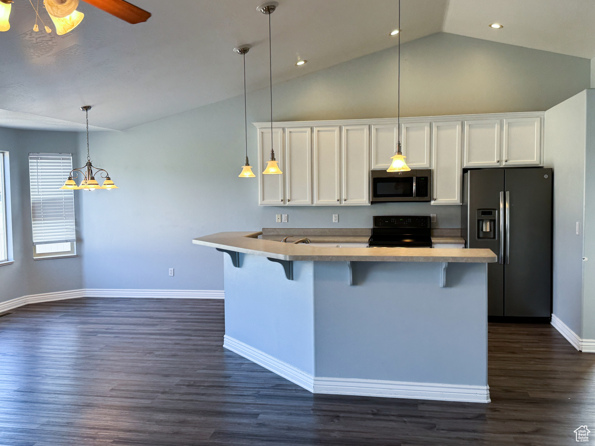 Kitchen with a breakfast bar, white cabinets, light countertops, appliances with stainless steel finishes, and decorative light fixtures