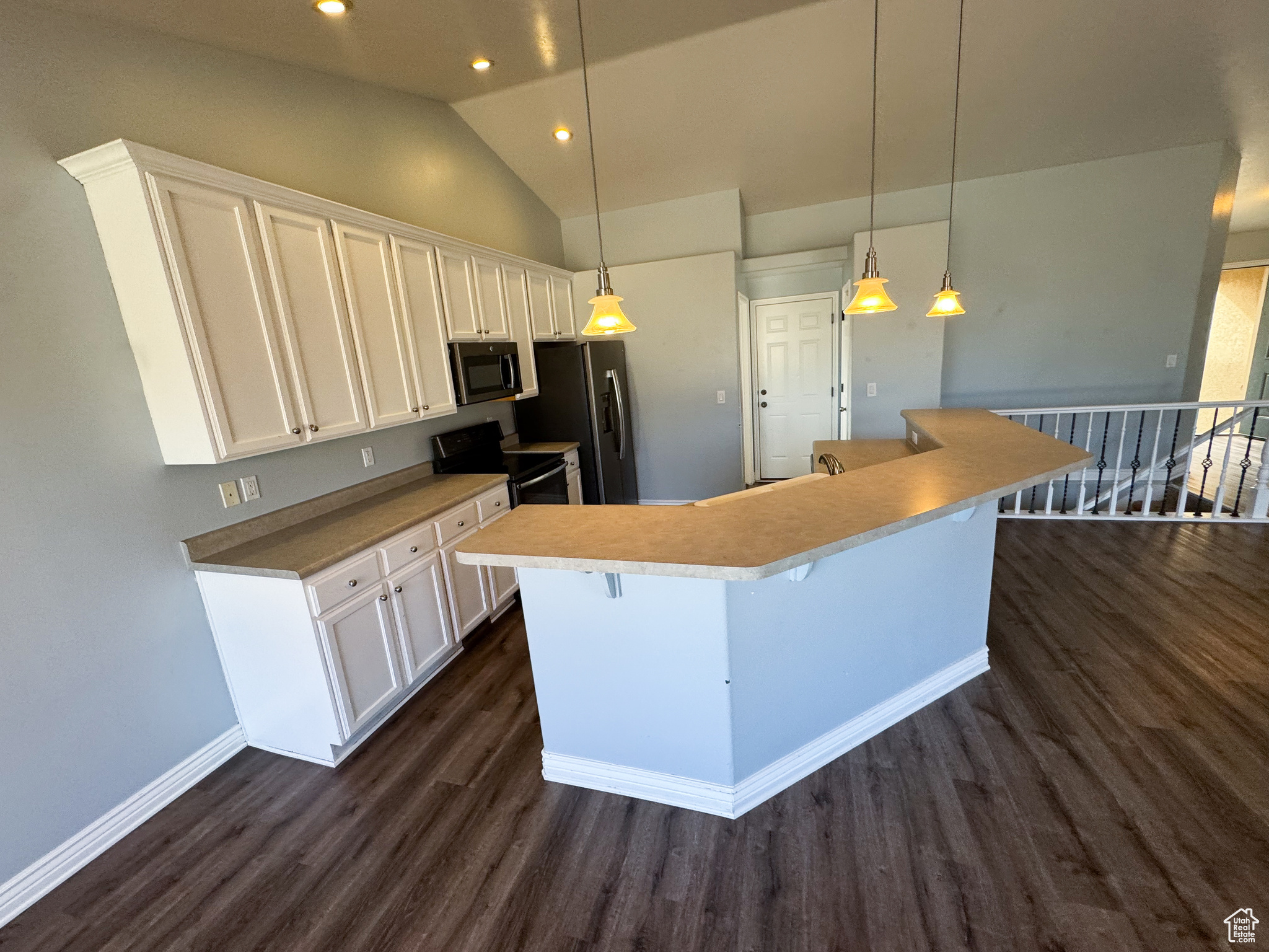 Kitchen featuring dark wood finished floors, a center island, stainless steel appliances, white cabinetry, and pendant lighting