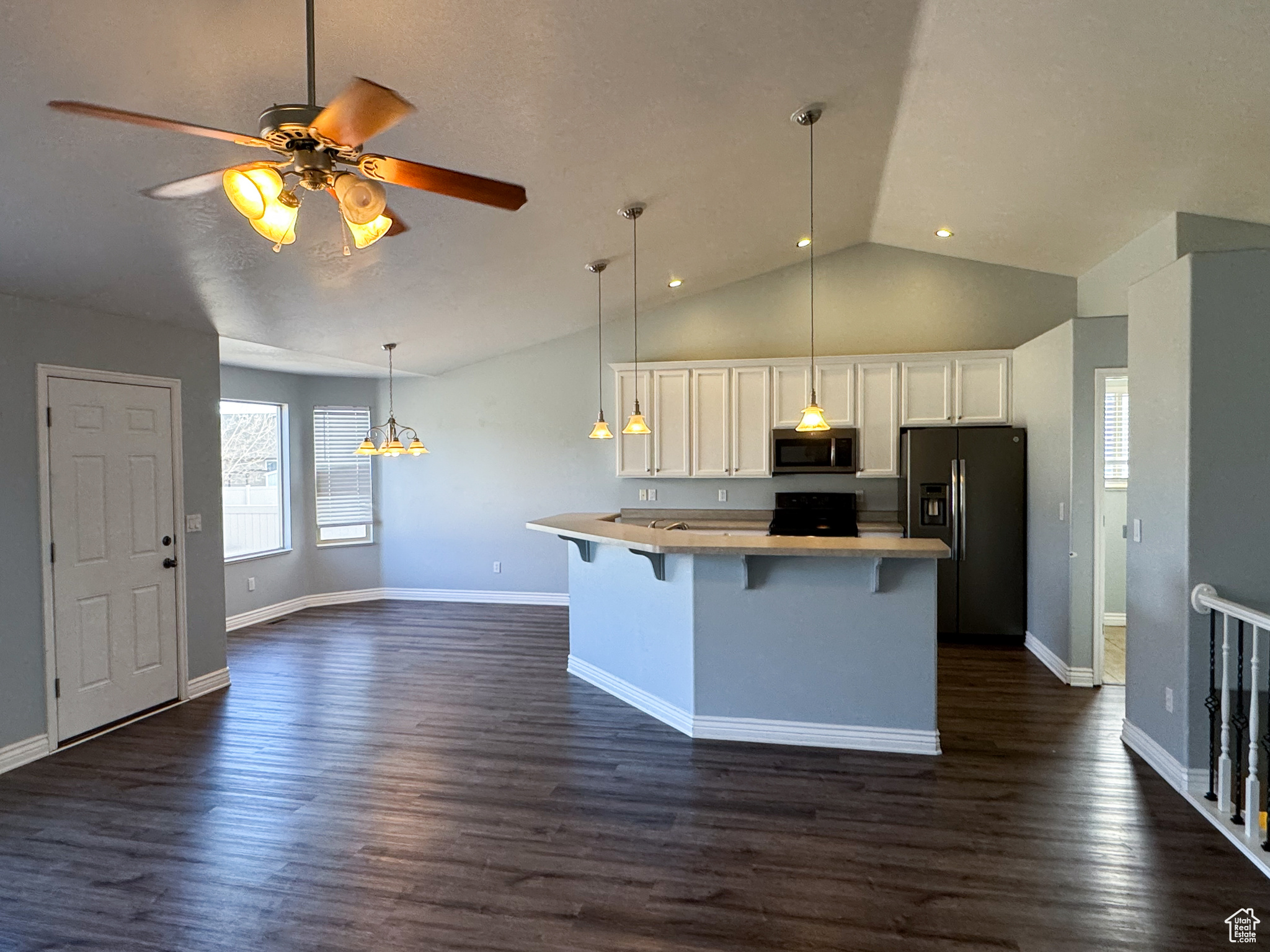 Kitchen featuring a breakfast bar area, decorative light fixtures, light countertops, black appliances, and white cabinetry