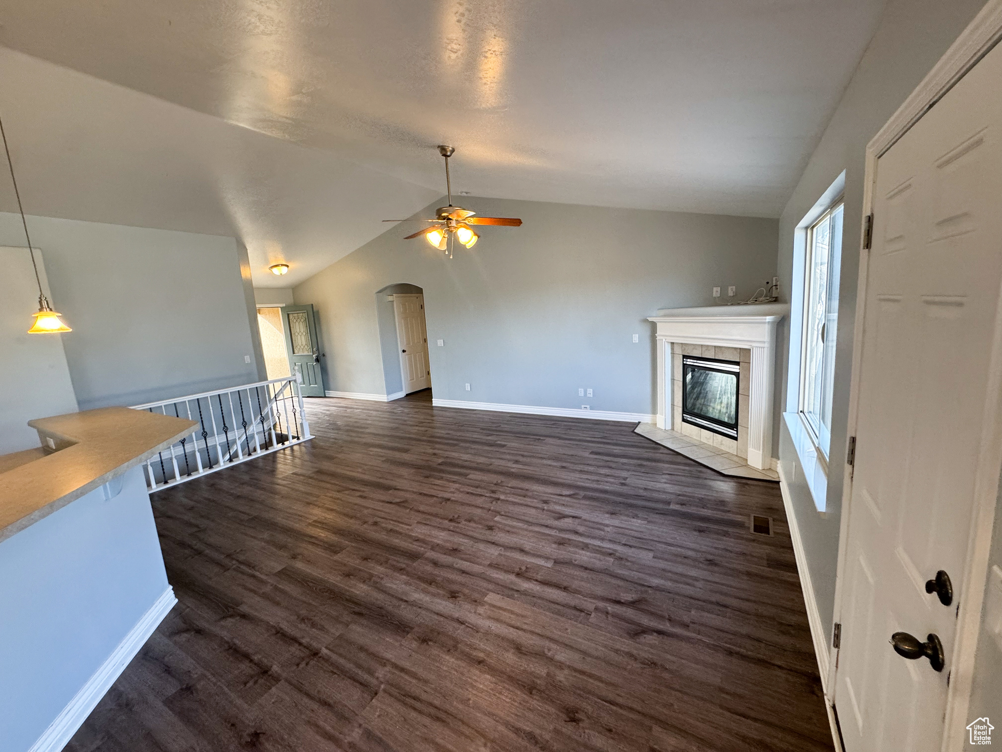 Unfurnished living room featuring arched walkways, dark wood finished floors, a fireplace, vaulted ceiling, and baseboards