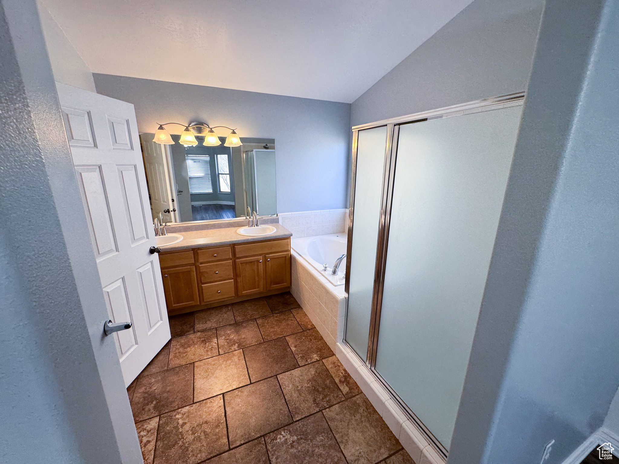 Bathroom featuring double vanity, a garden tub, vaulted ceiling, a shower stall, and a sink