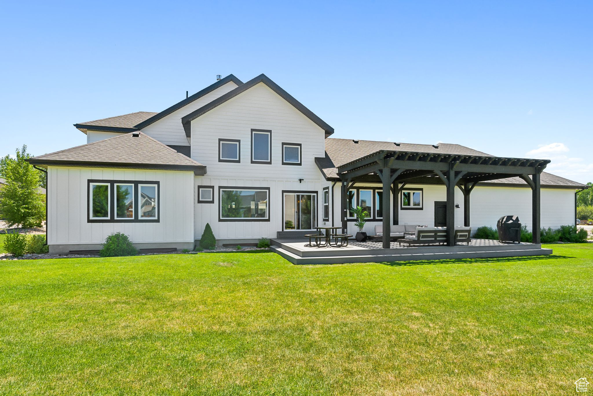 Rear view of house featuring board and batten siding, a shingled roof, a lawn, and a pergola