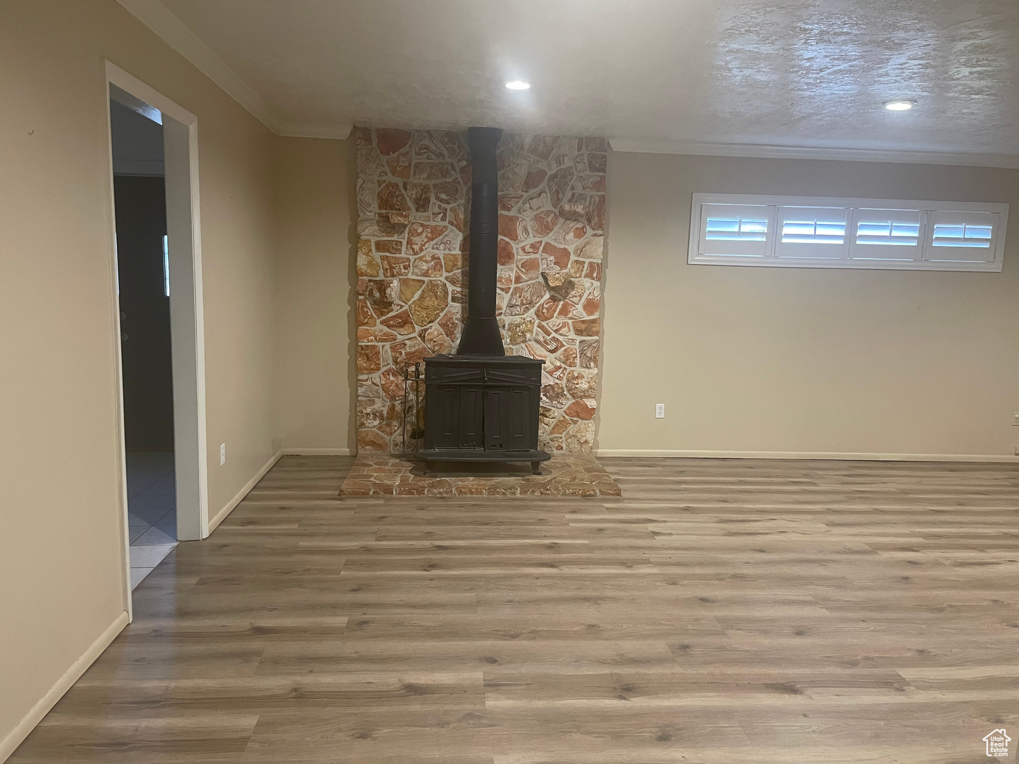Unfurnished living room with hardwood / wood-style flooring, crown molding, a textured ceiling, and a wood stove