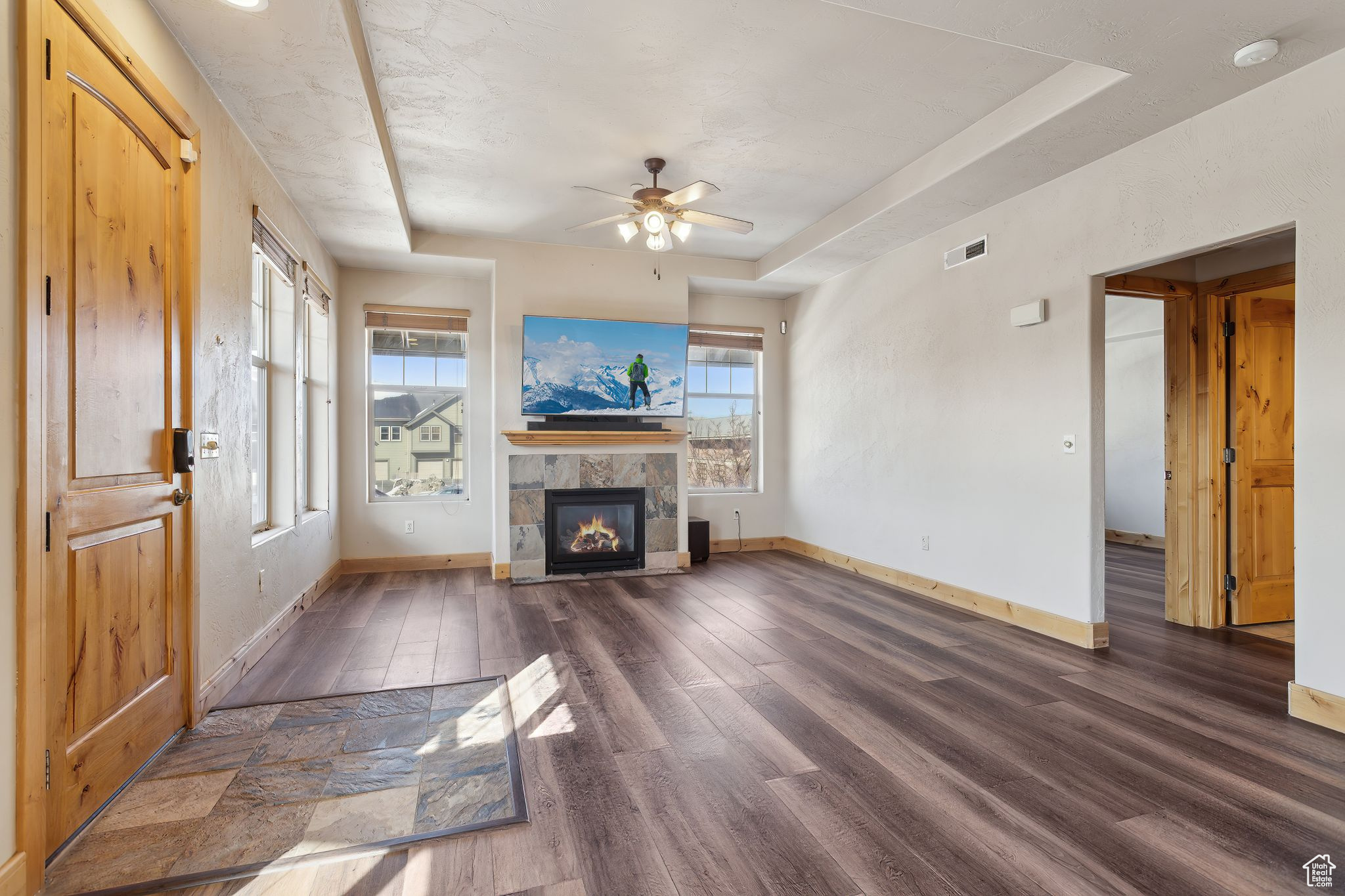 Living room featuring gas fireplace LVT flooring, a tray ceiling with ceiling fan