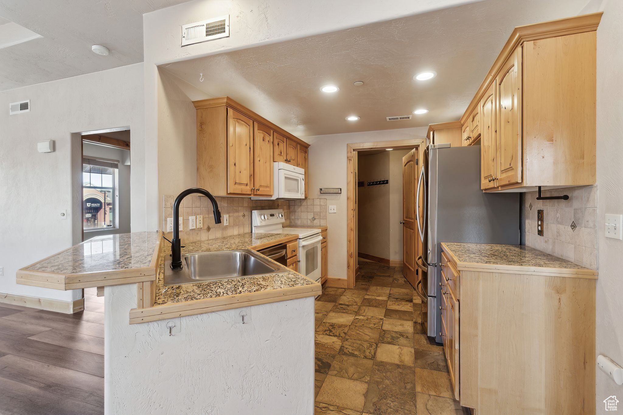 Kitchen featuring white microwave, a peninsula, granite countertops, freestanding refrigerator, and a kitchen bar