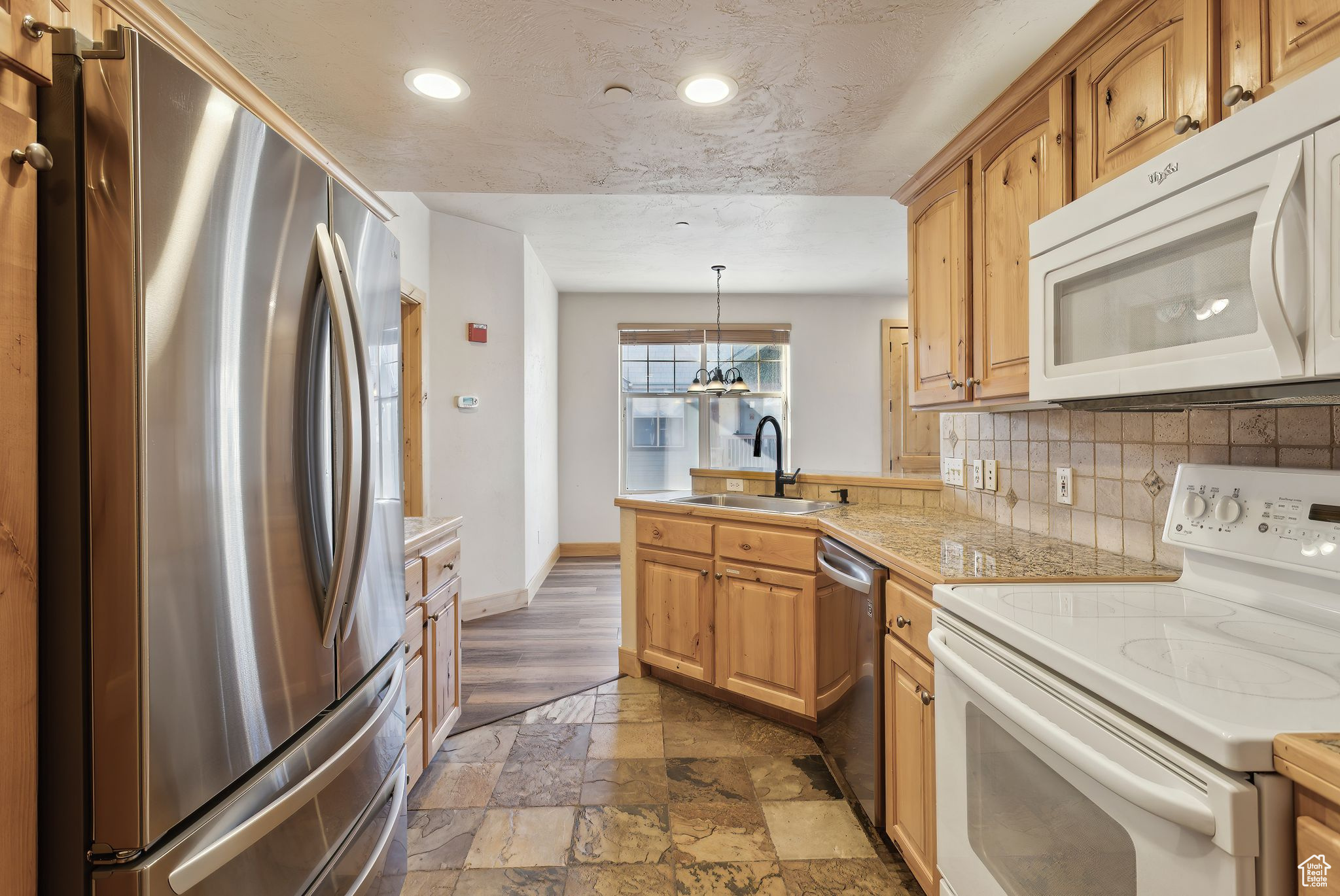 Kitchen featuring white microwave, a peninsula, granite countertops, freestanding refrigerator, and a kitchen bar