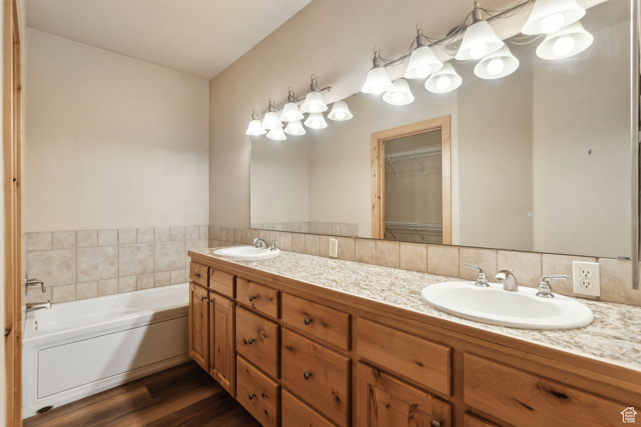 Full bathroom with double vanity, wood finished floors, a tub, separate shower, and a walk in closet