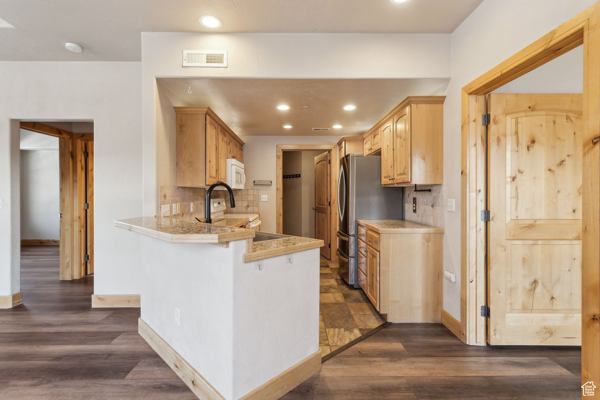 Kitchen featuring white microwave, a peninsula, granite countertops, freestanding refrigerator, and a kitchen bar