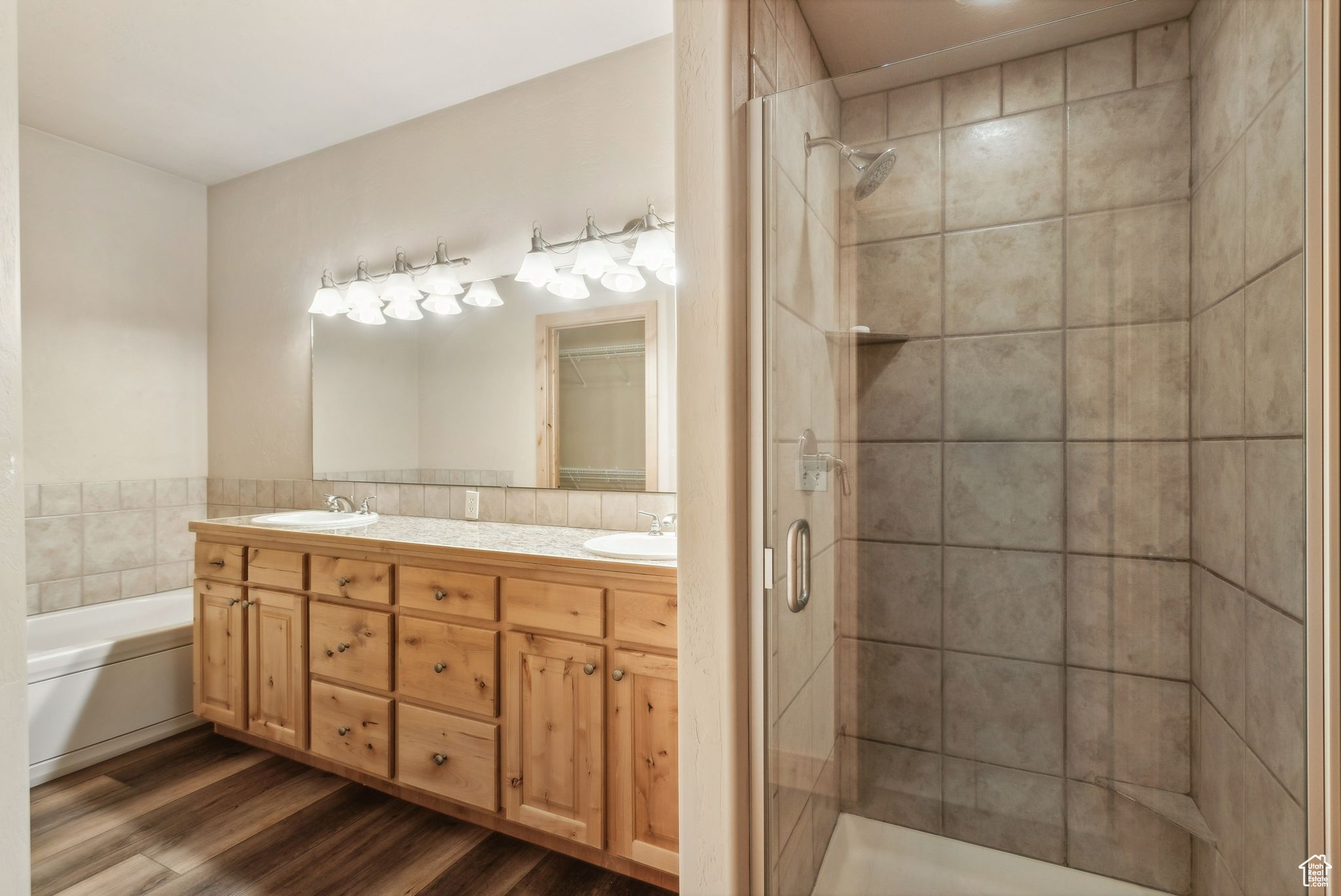 Full bathroom with double vanity, wood finished floors, a tub, separate shower, and a walk in closet