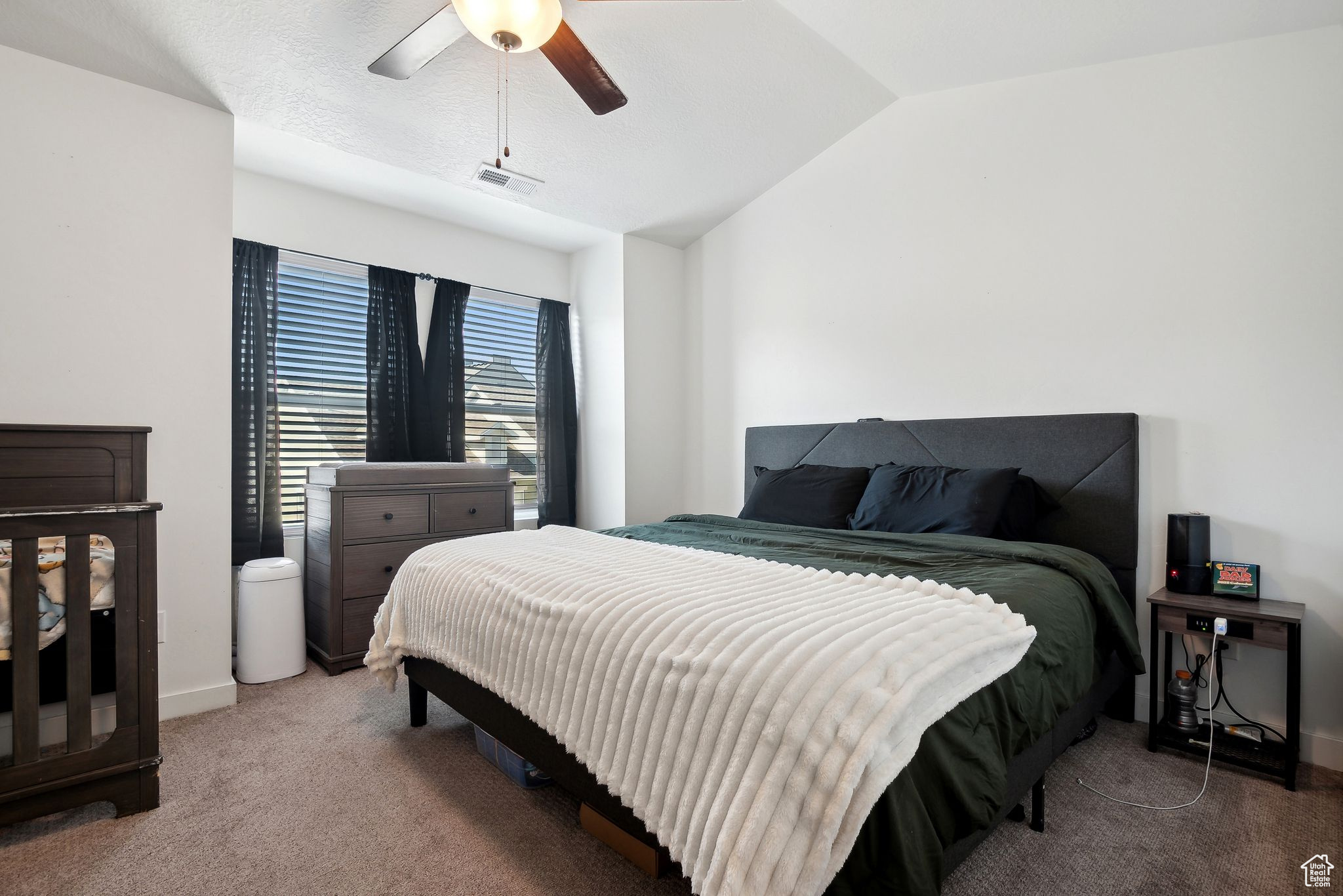 Carpeted bedroom with a ceiling fan, visible vents, vaulted ceiling, and baseboards