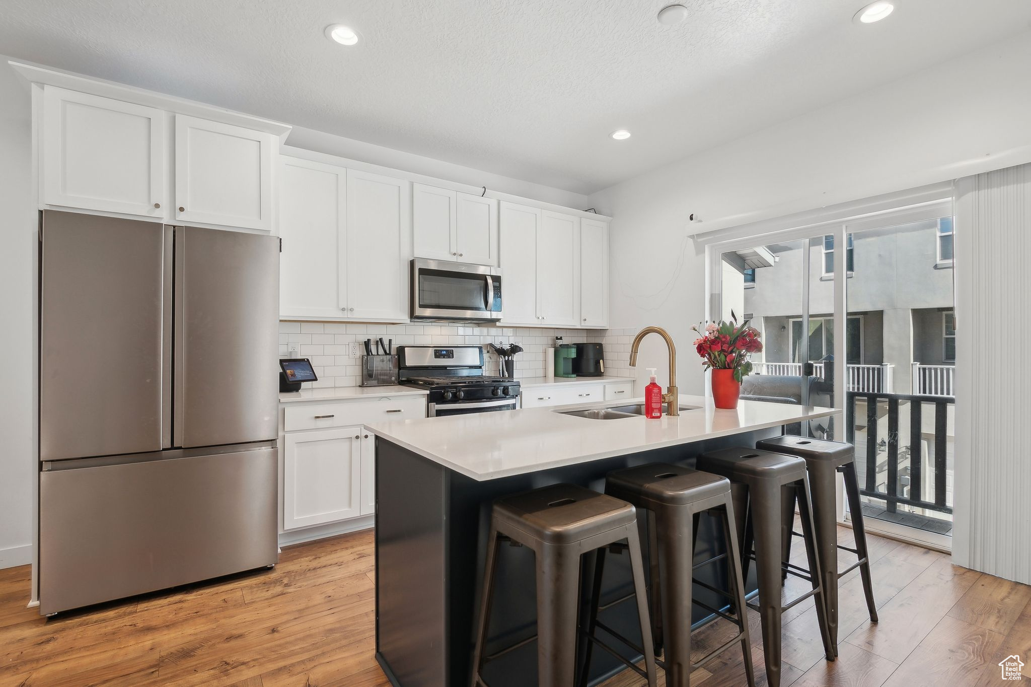 Kitchen with a center island with sink, light countertops, appliances with stainless steel finishes, white cabinets, and a sink