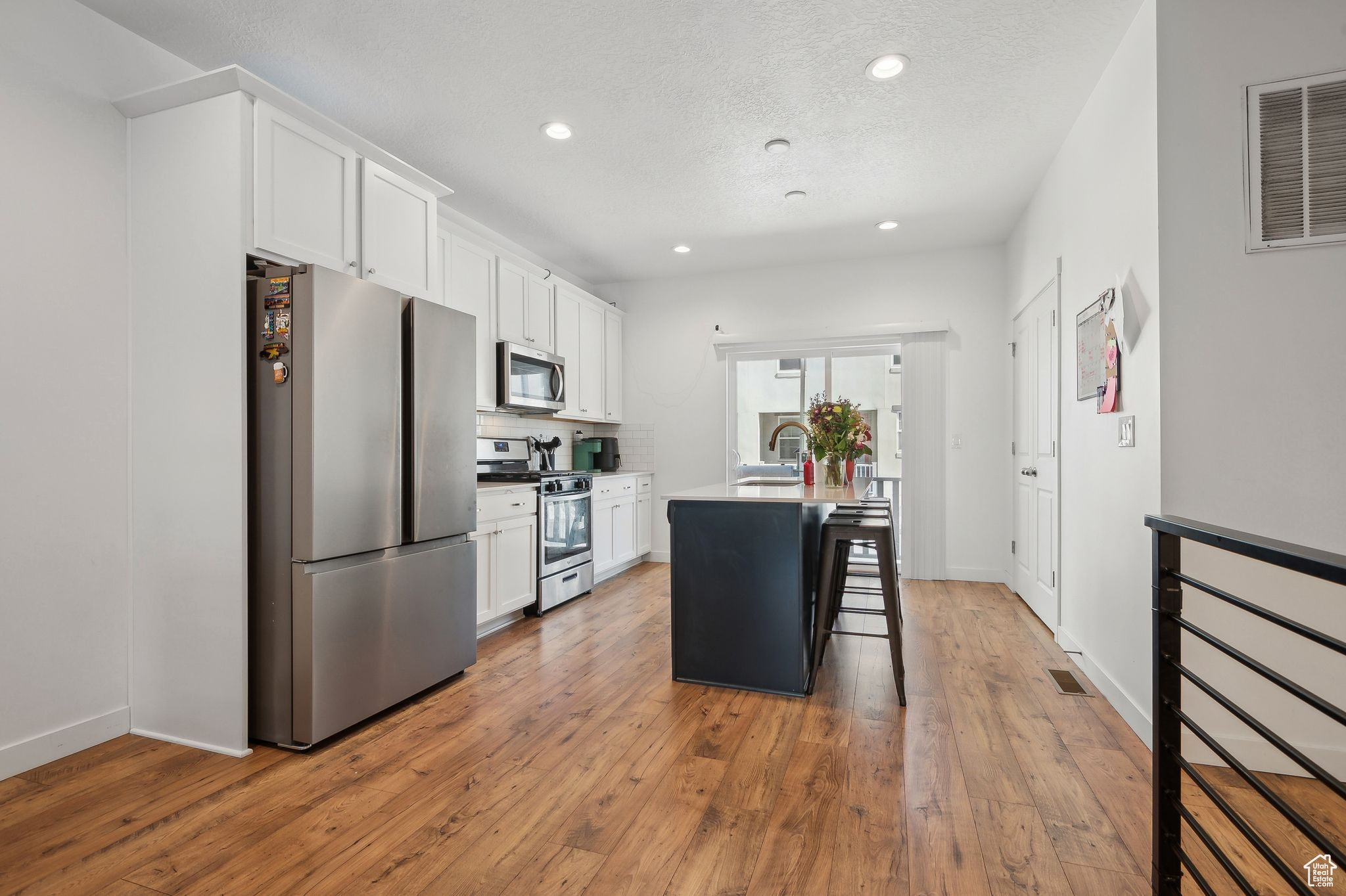 Kitchen with visible vents, a breakfast bar area, a kitchen island with sink, stainless steel appliances, and white cabinetry