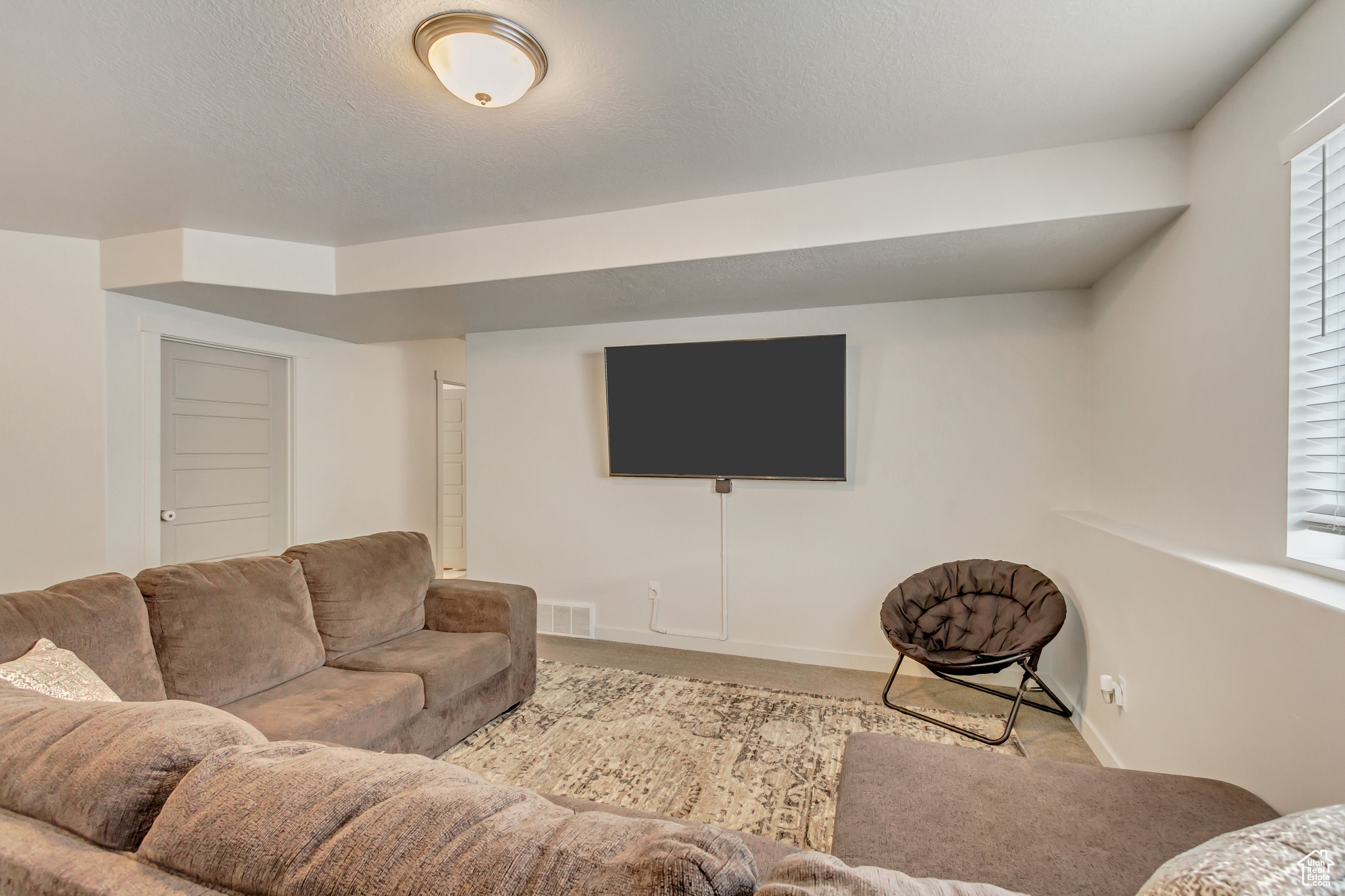 Living area with light colored carpet, visible vents, baseboards, and a textured ceiling
