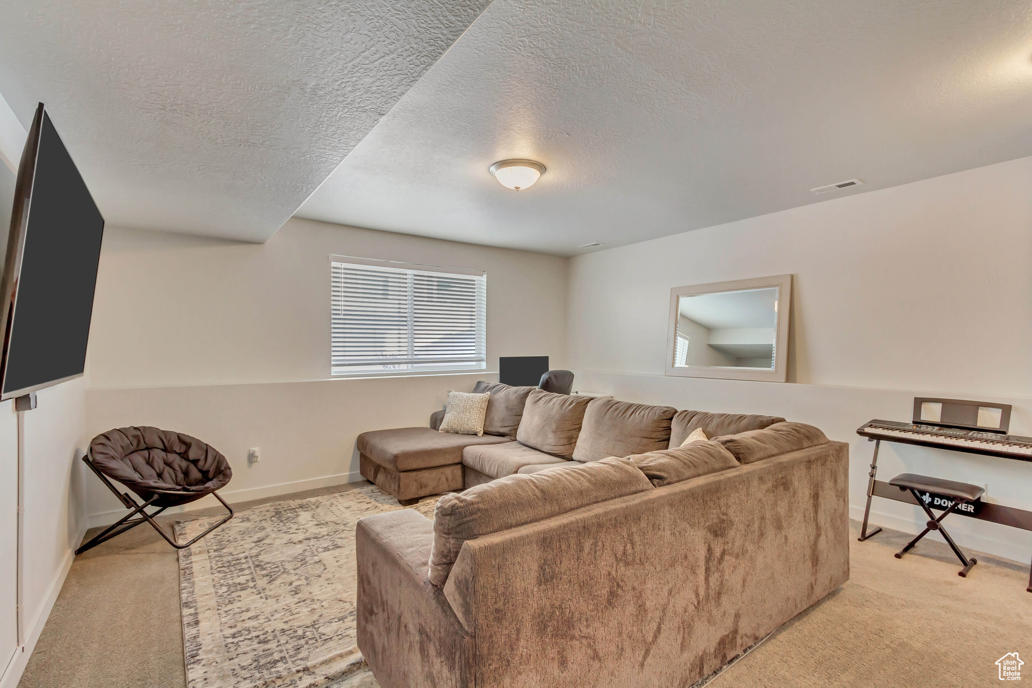 Living room with a textured ceiling, baseboards, visible vents, and light colored carpet
