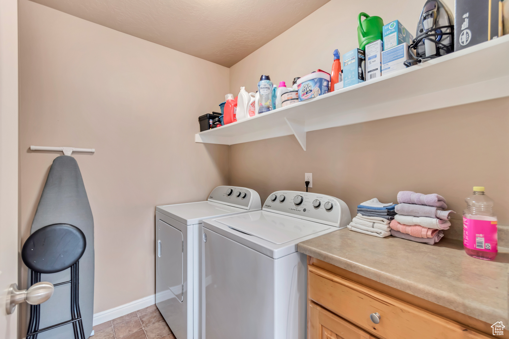 Clothes washing area featuring light tile patterned floors, baseboards, washer and dryer, and counter and drawer storage