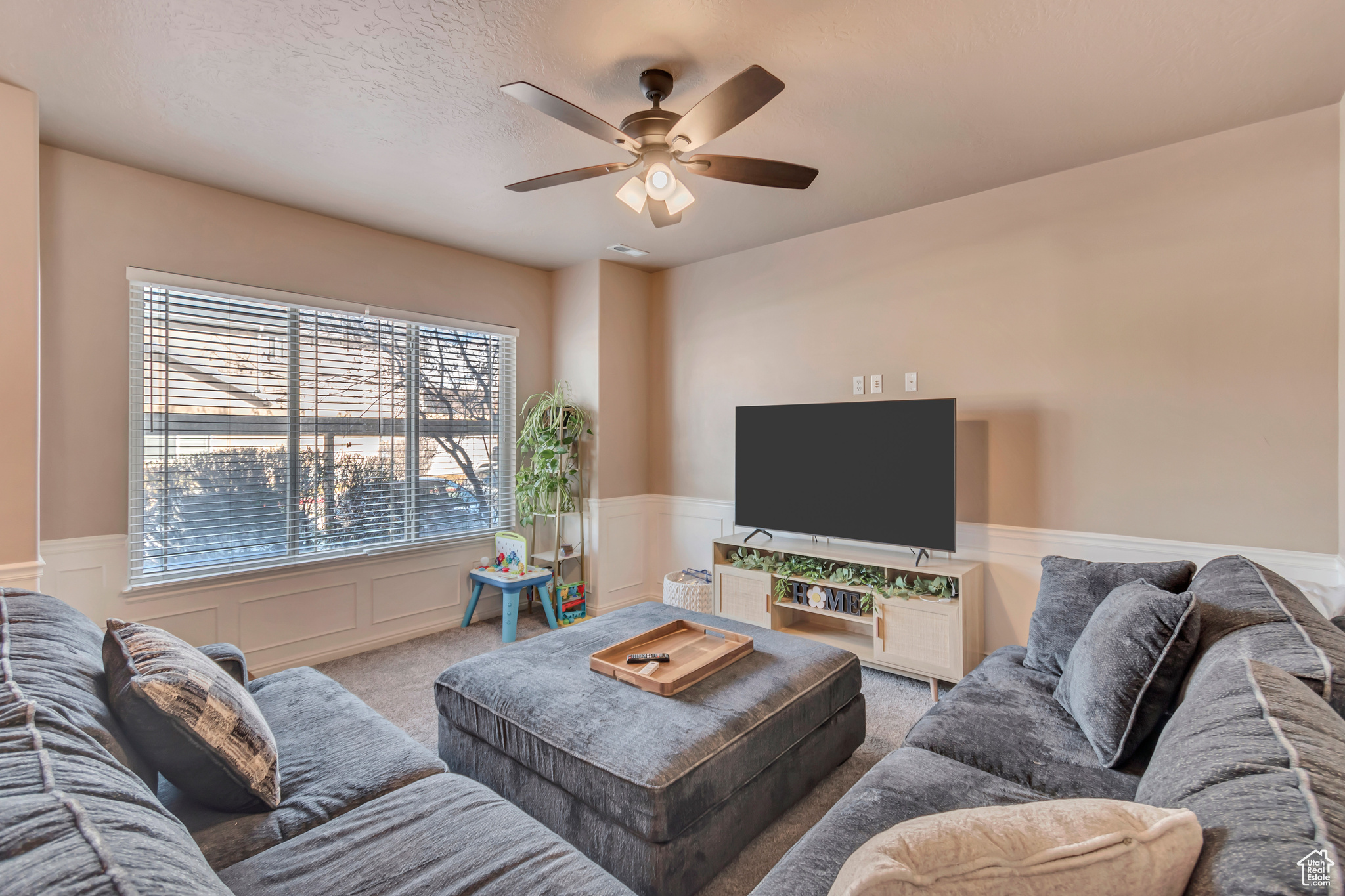 Carpeted living area with a ceiling fan, wainscoting, and a textured ceiling