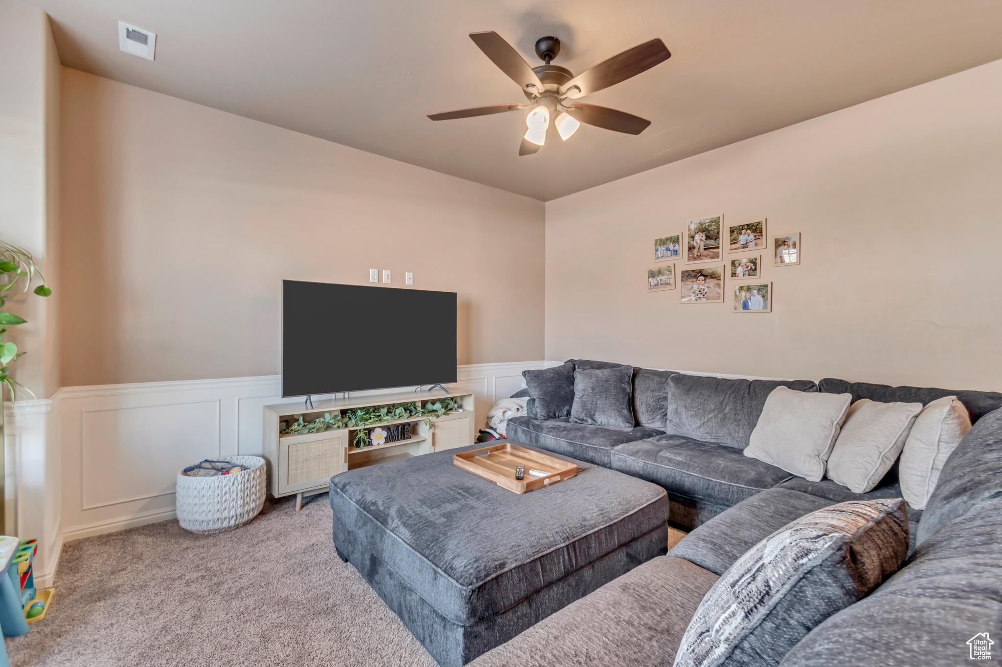 Living area featuring a ceiling fan, carpet, and wainscoting