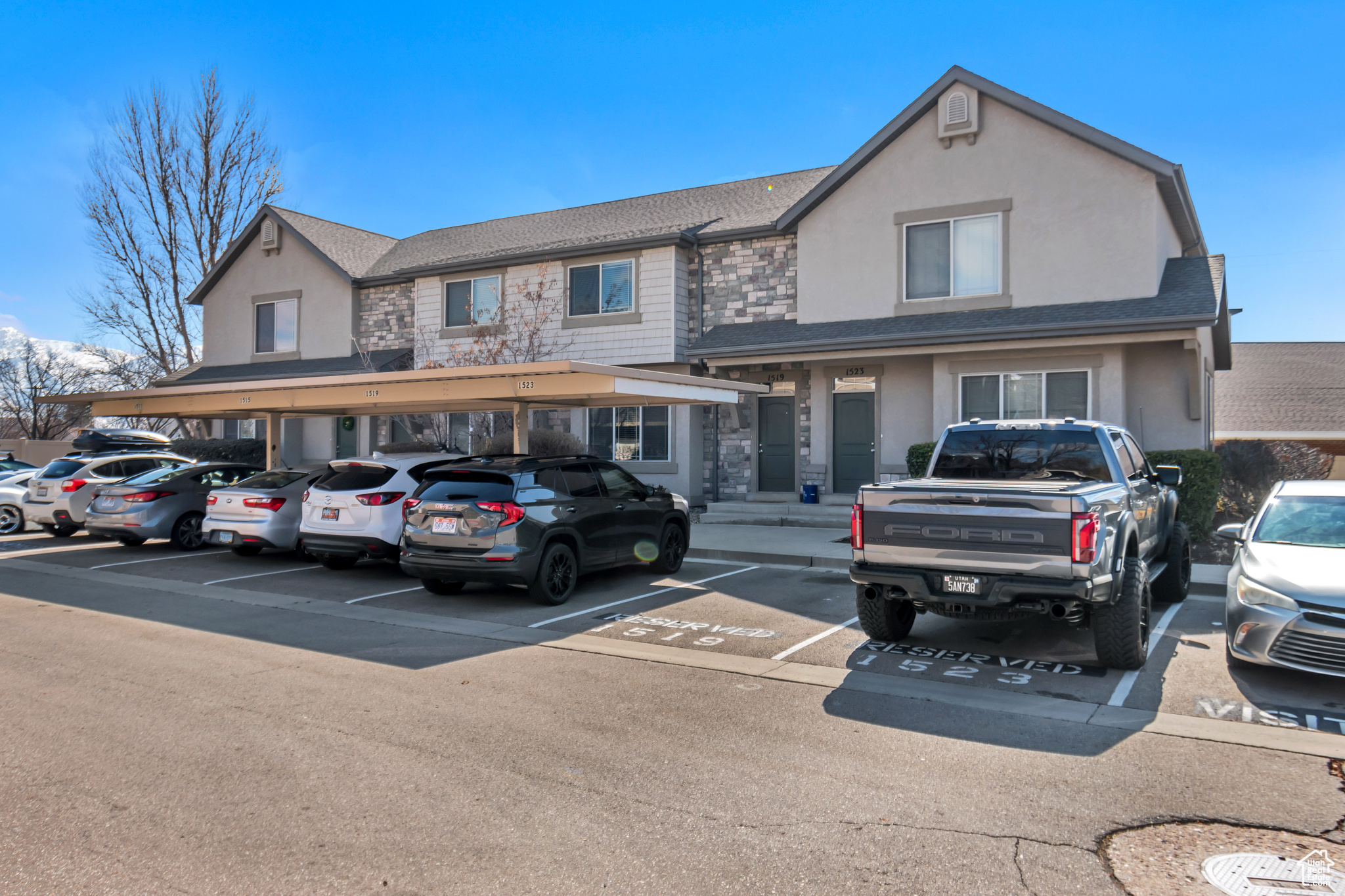 View of front of home featuring stone siding, stucco siding, and covered and uncovered parking