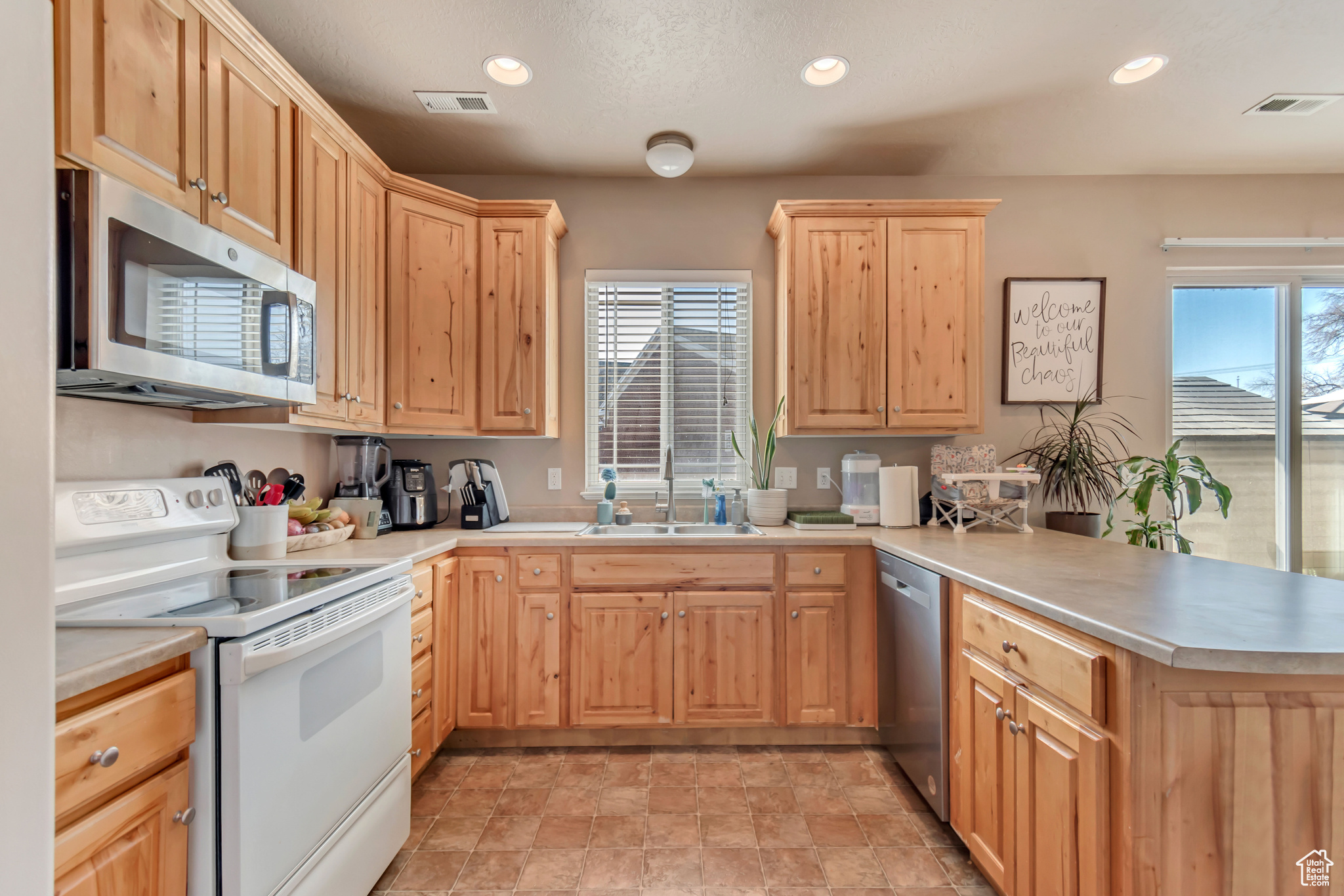 Kitchen with light brown cabinetry, a peninsula, stainless steel appliances, and a sink