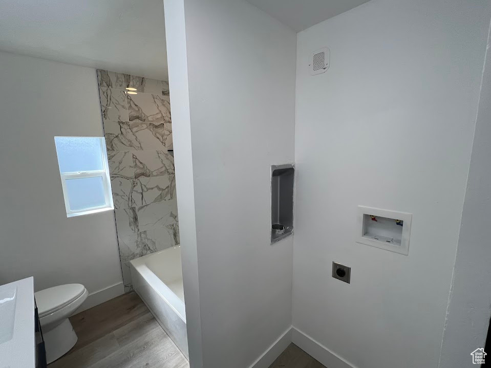 Bathroom with toilet, baseboards,  shower combination, and wood finished floors
