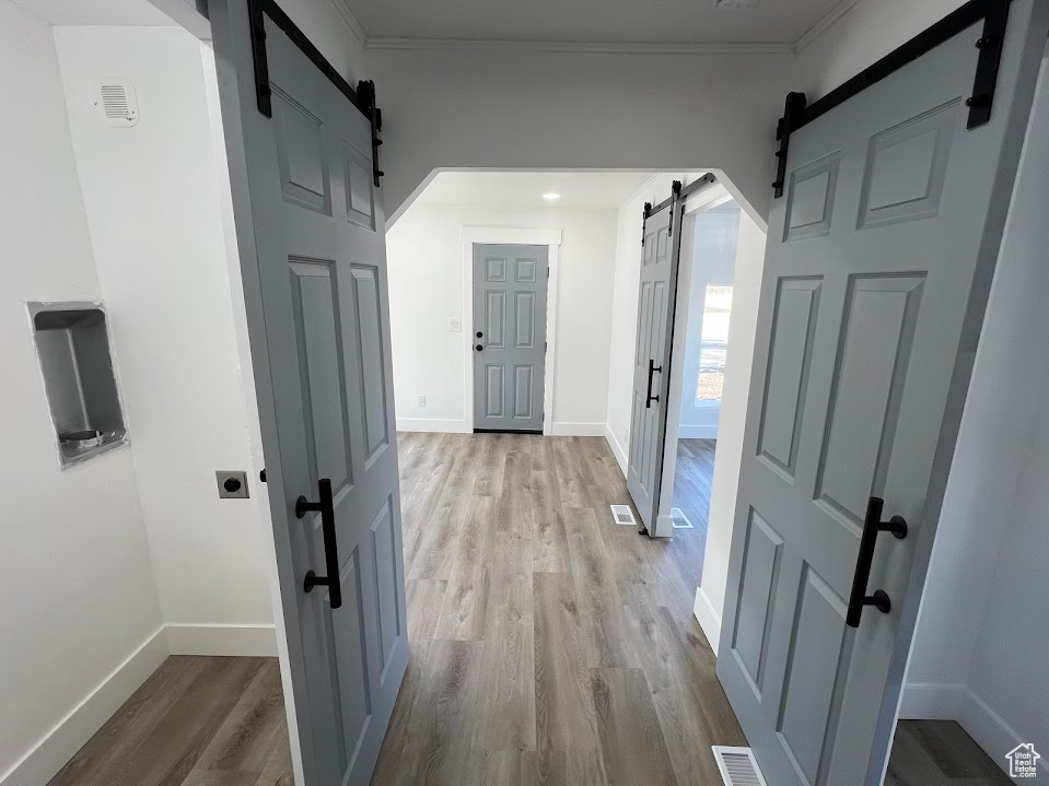 Corridor featuring a barn door, light wood-style flooring, visible vents, baseboards, and ornamental molding