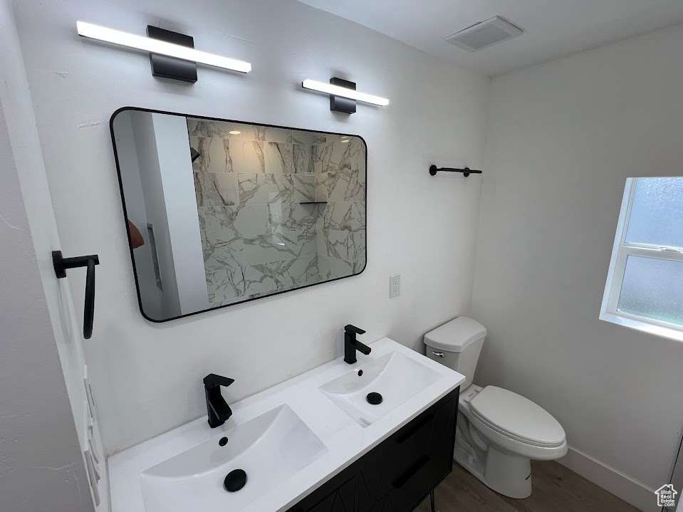 Full bath with toilet, double vanity, visible vents, and a sink