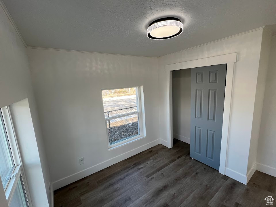 Unfurnished bedroom with a closet, dark wood-style flooring, a textured ceiling, and baseboards