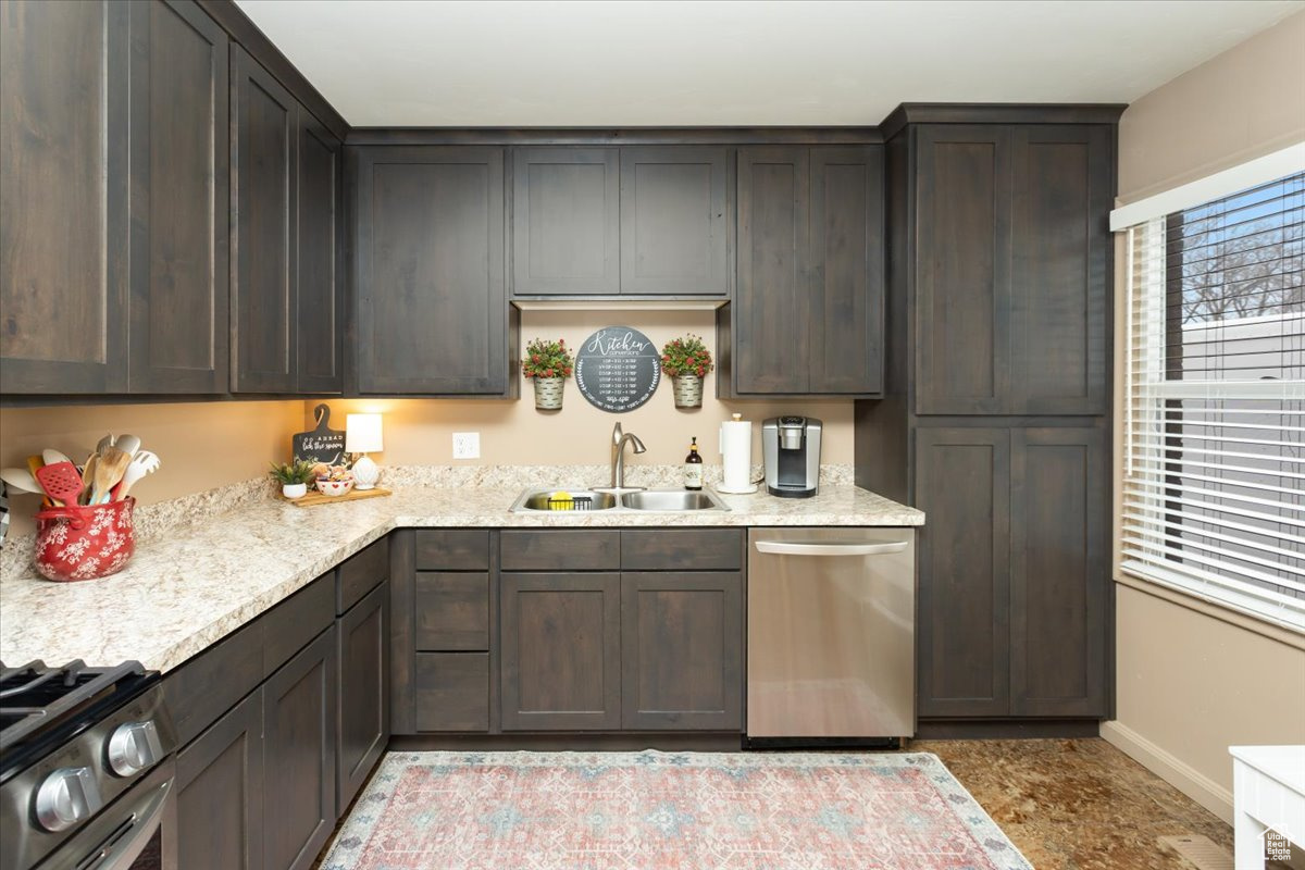 Kitchen featuring dark brown cabinetry, sink, light stone counters, and appliances with stainless steel finishes