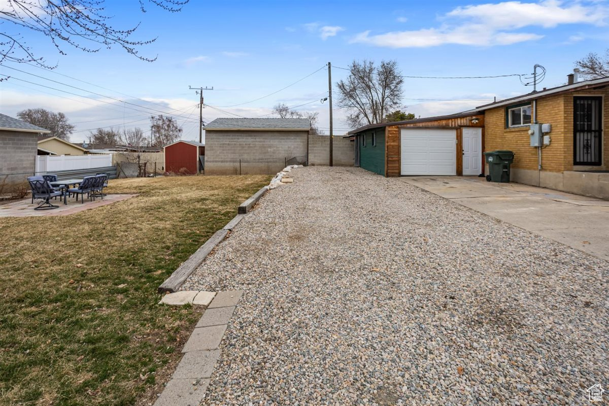 View of yard featuring concrete driveway, a patio, an outbuilding, an attached garage, and fence