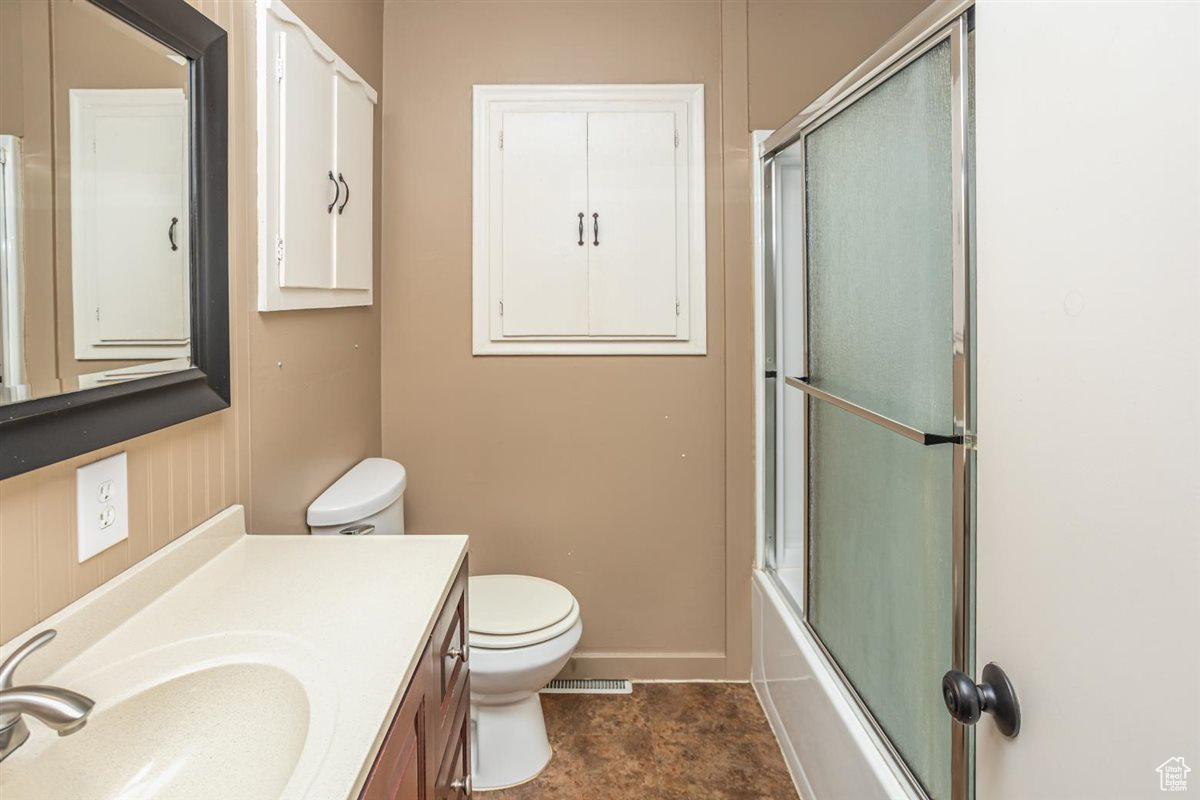 Full bath featuring shower / bath combination with glass door, visible vents, toilet, vanity, and baseboards